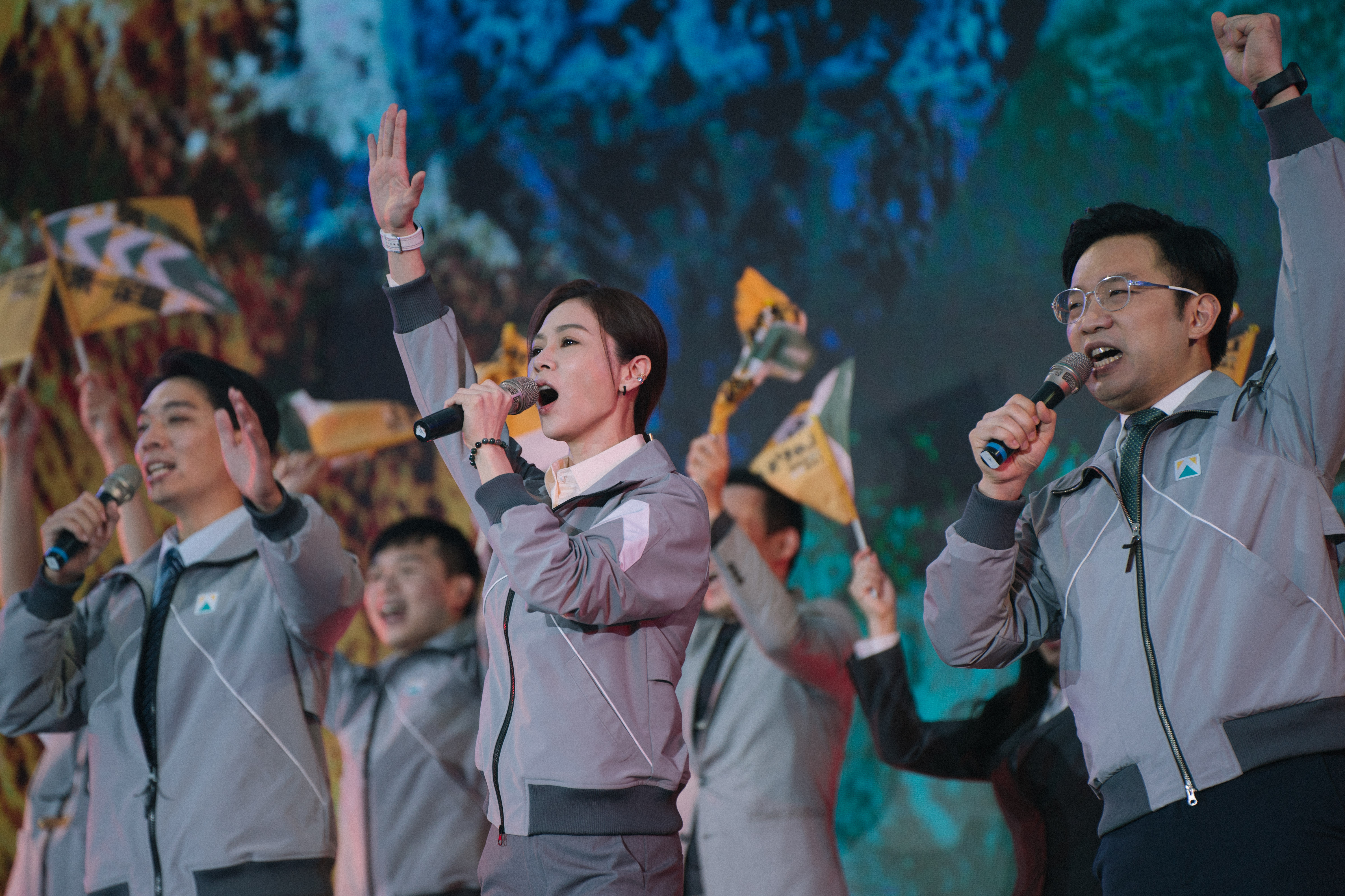 A scene from the Netflix show Wave Makers. A woman is in the middle on a stage at a political rally and raising her fist into the air. Others are following her lead.