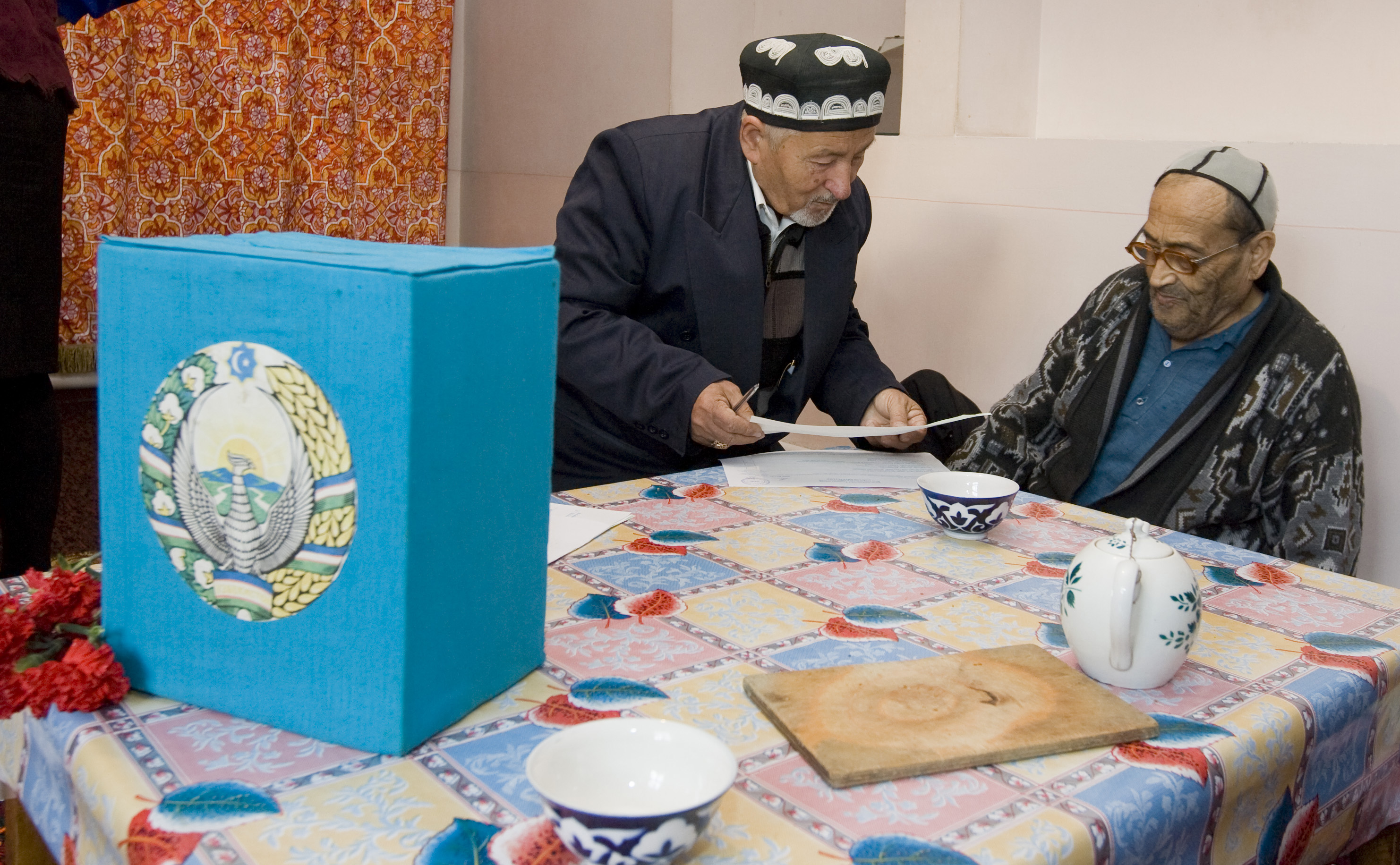 A visiting member of a local election committee (L) shows a ballot to a man at his home during a parliamentary election in Tashkent