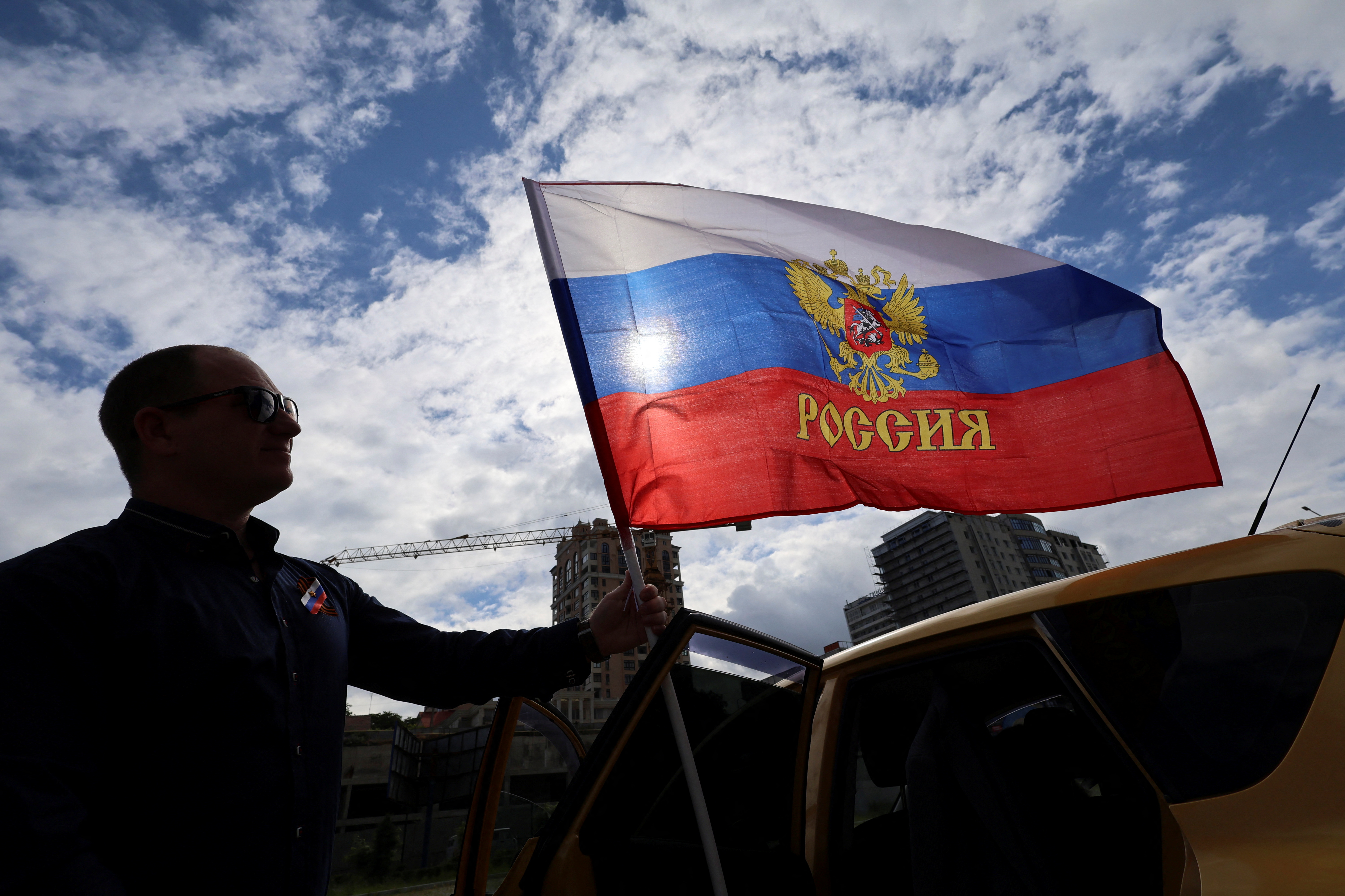 A participant attaches a flag to his car before an automobile rally marking Russia Day in Sevastopol, Crimea, June 12, 2023.