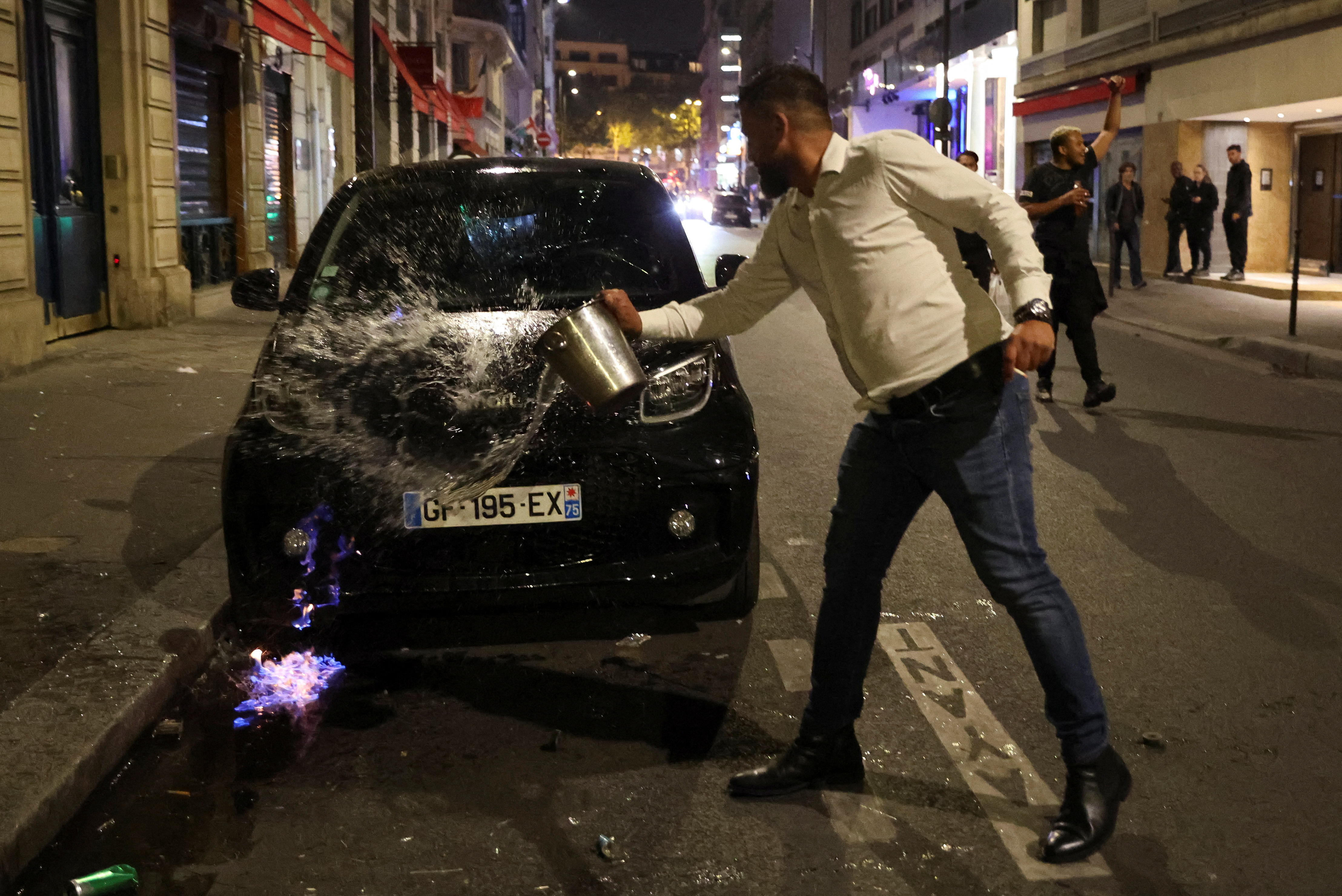 A man drops water to extinguish flames during protests following the death of Nahel, a 17-year-old teenager killed by a French police officer in Nanterre during a traffic stop, in Paris