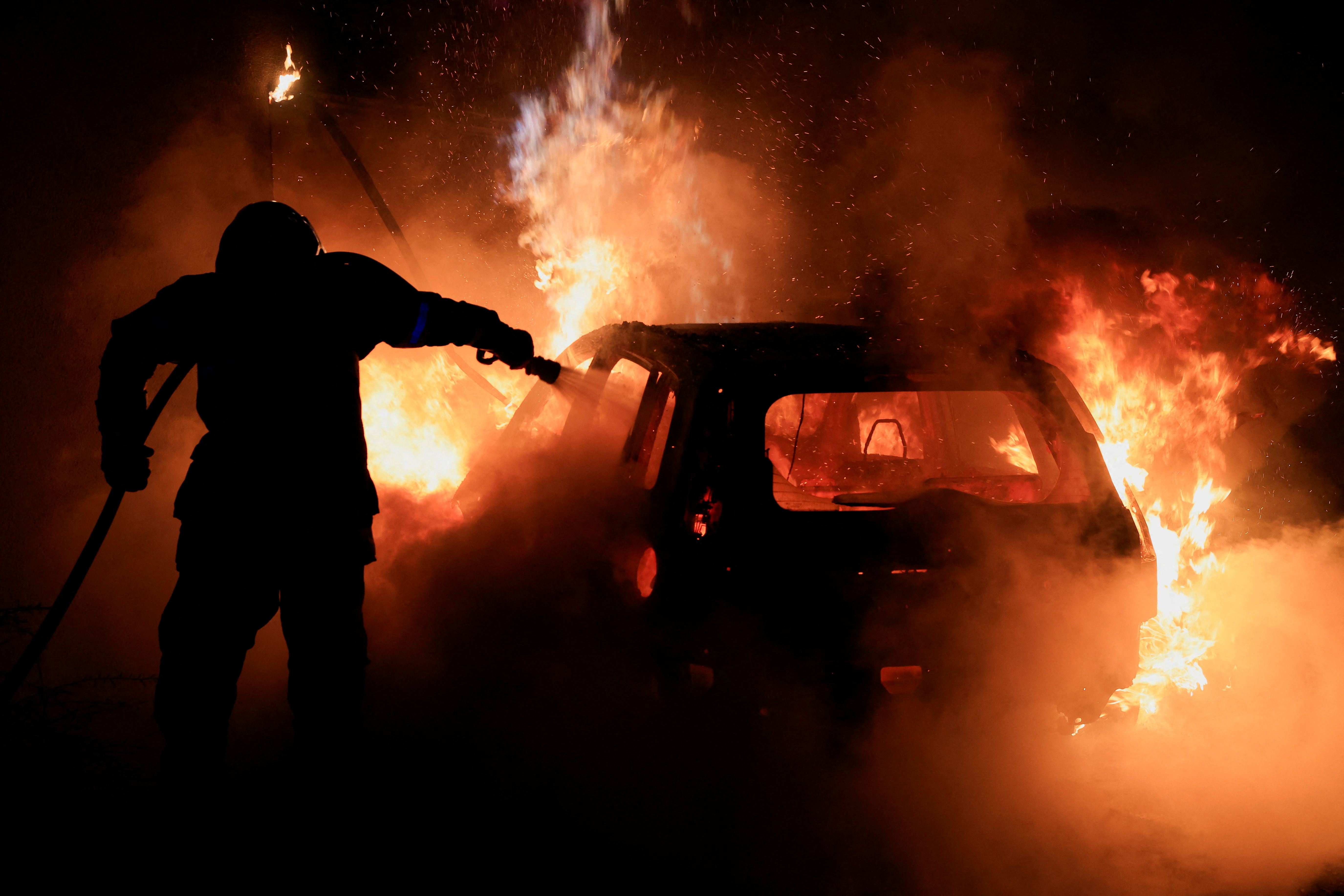 A French firefighter works to extinguish a burning car during the fifth day of protests following the death of Nahel,