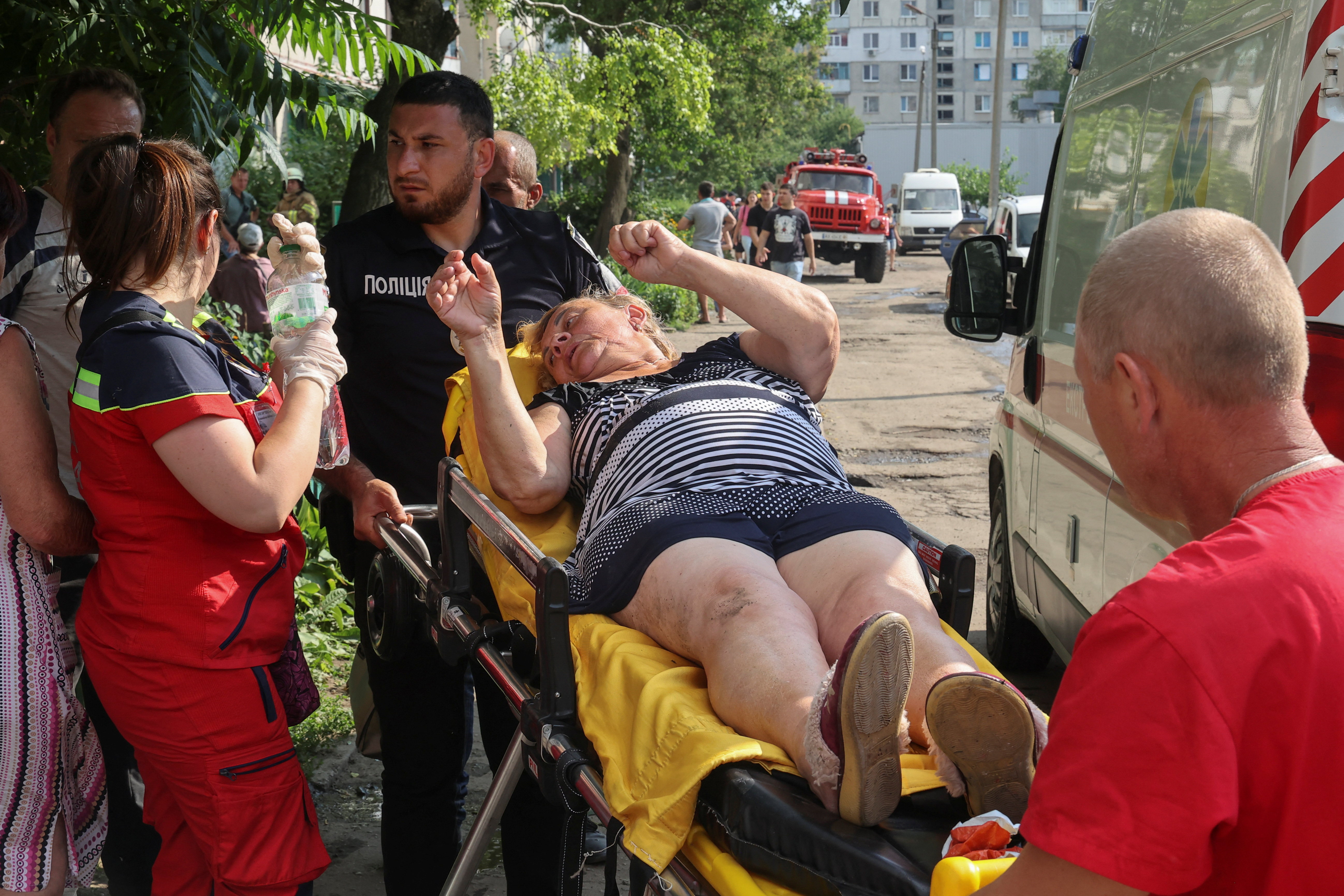 An injured woman being taken away on a stretcher after a missile hit a residential area in Pervomaiskyi. She is gesturing to another person.