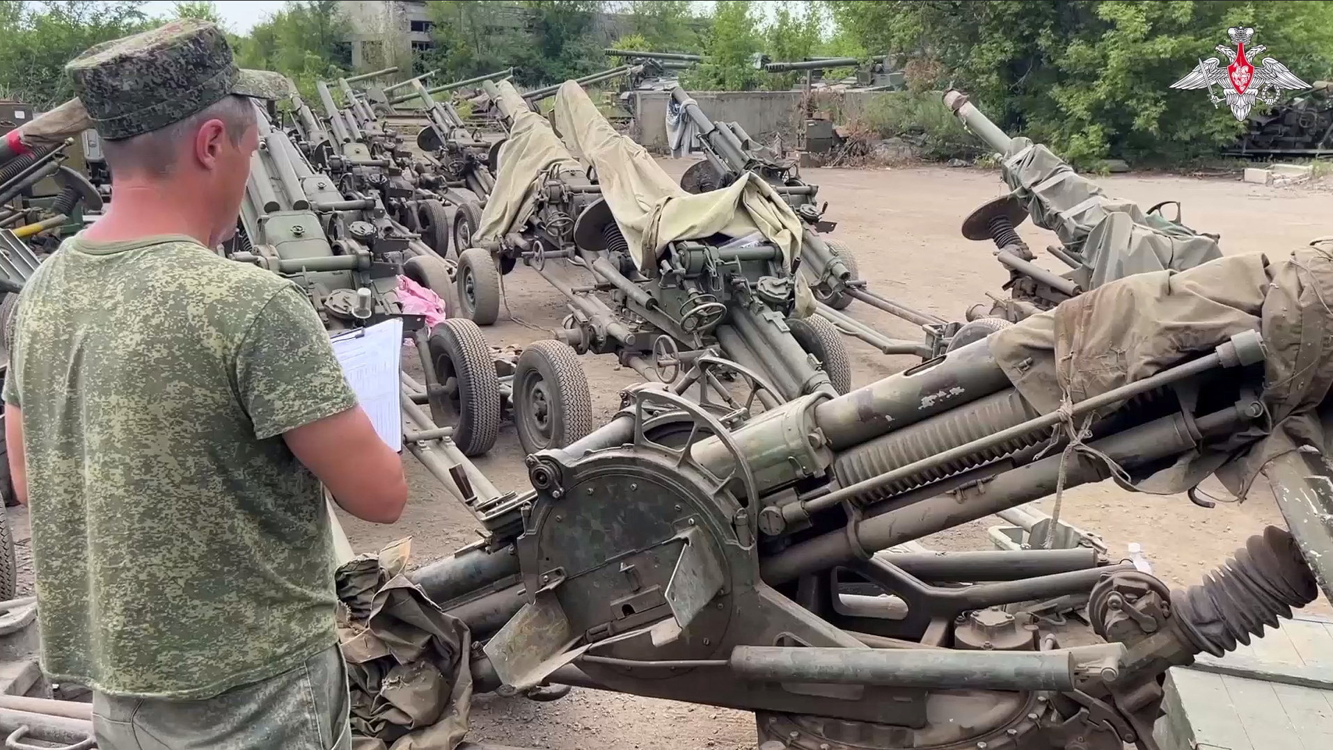 A military official checking howitzers transferred from the Wagner group. He has a clip board and is writing.