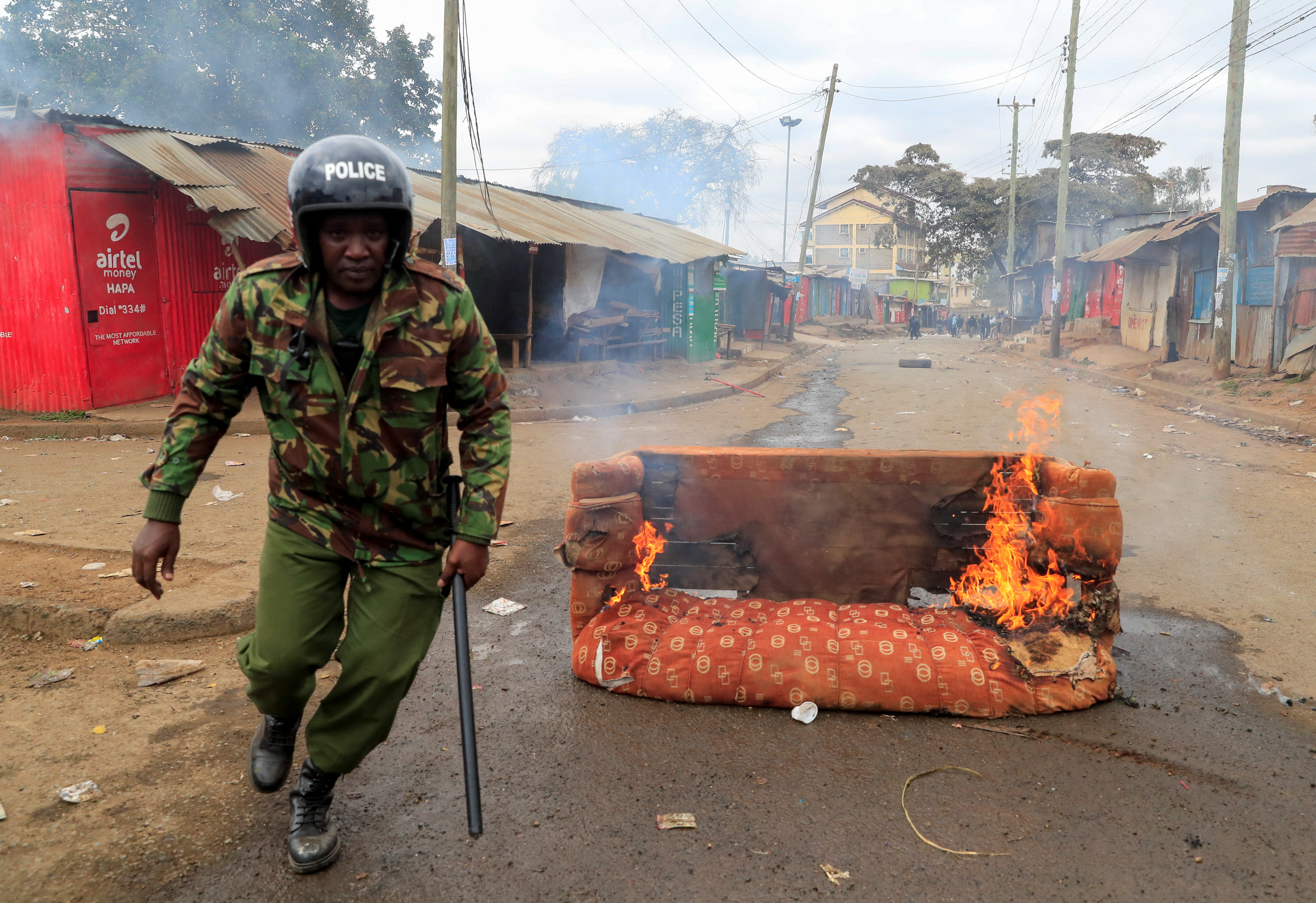 A riot police officer runs next to a burning sofa, as supporters of Kenya's opposition leader Raila Odinga of the Azimio La Umoja coalition participate in an anti-government protest against tax hikes by the government in Nairobi, Kenya