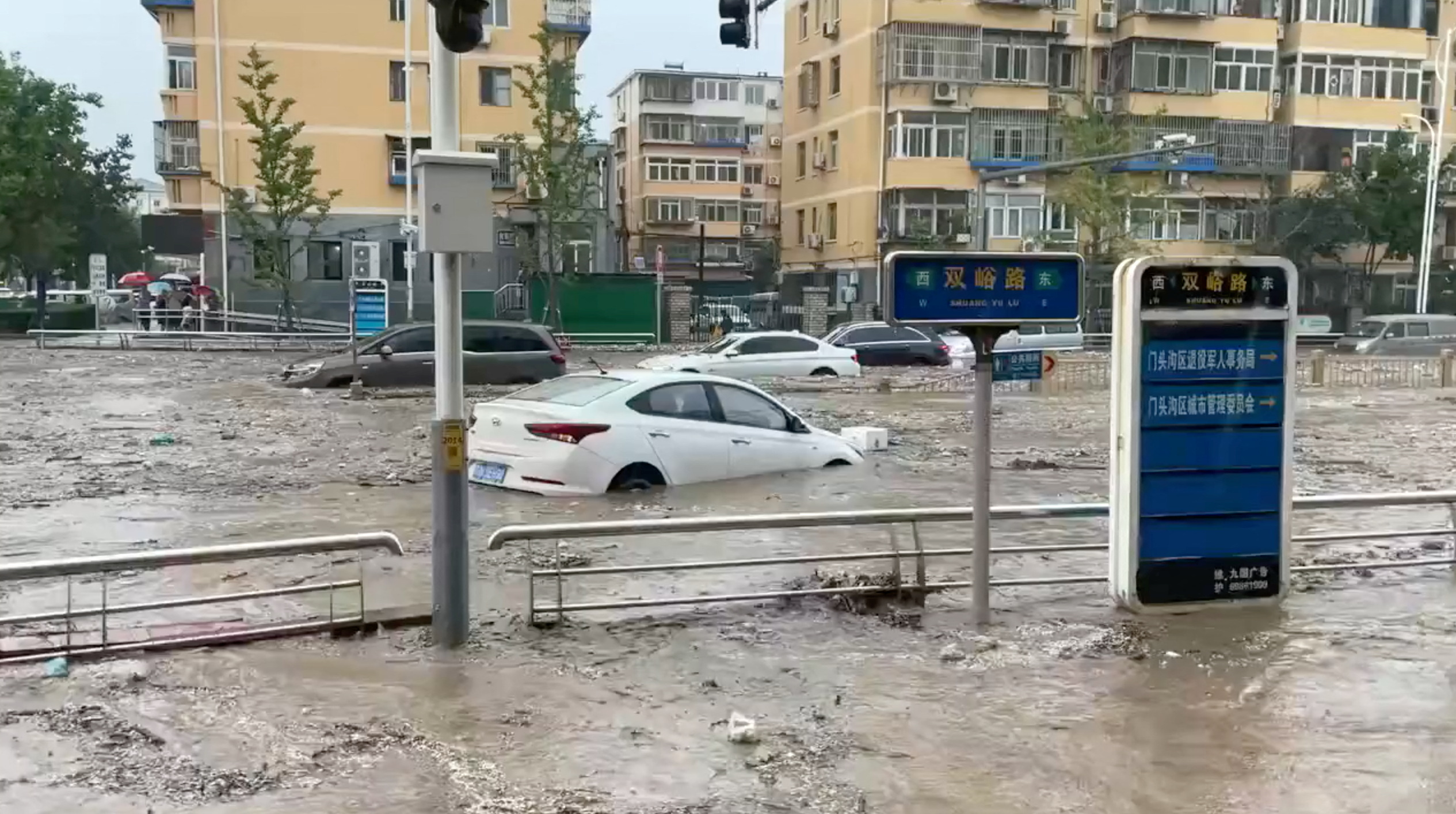 Cars are partially submerged as water gushes on a flooded street,