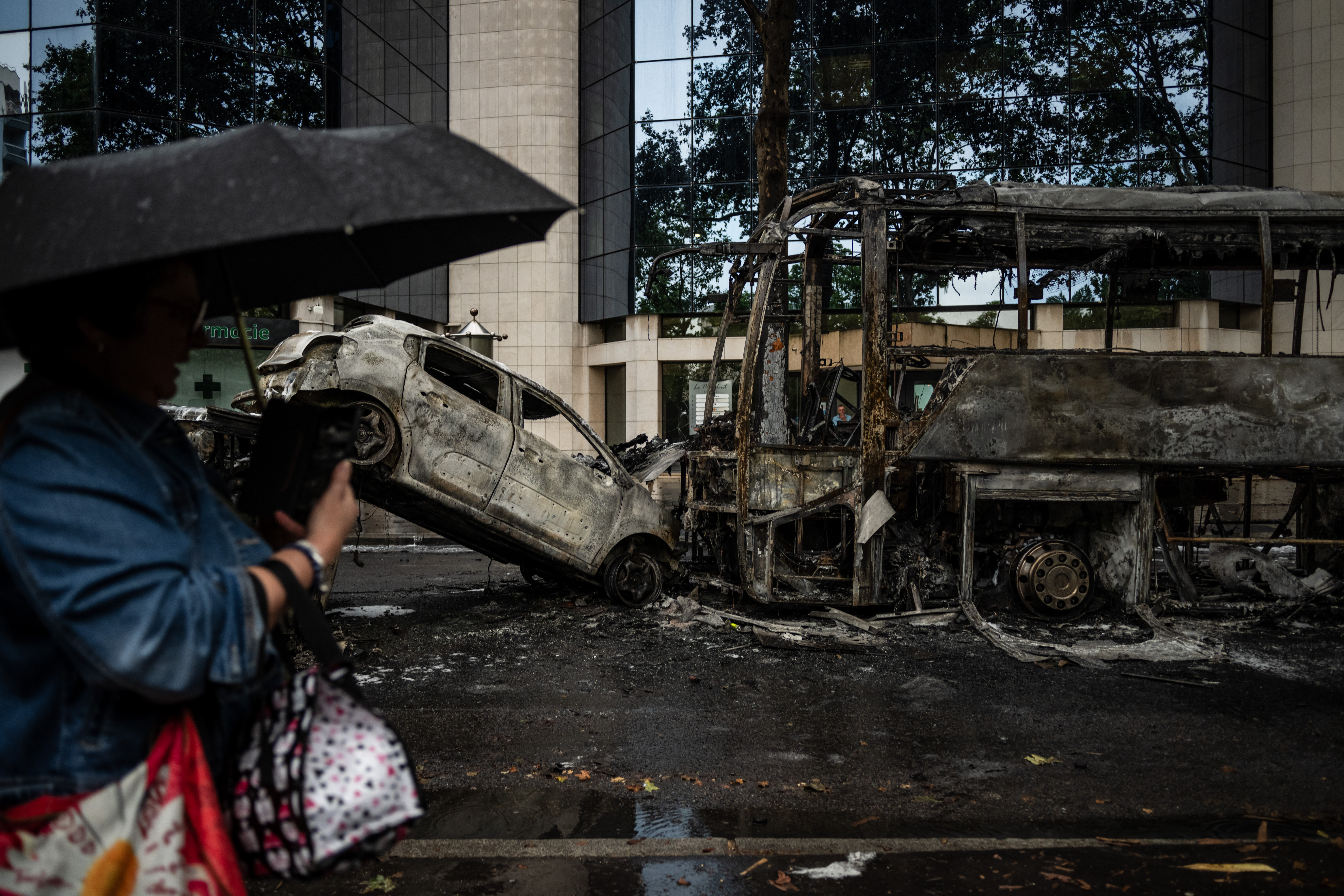 A pedestrian takes an image as she walks by burnt vehicles on a street in Lyon