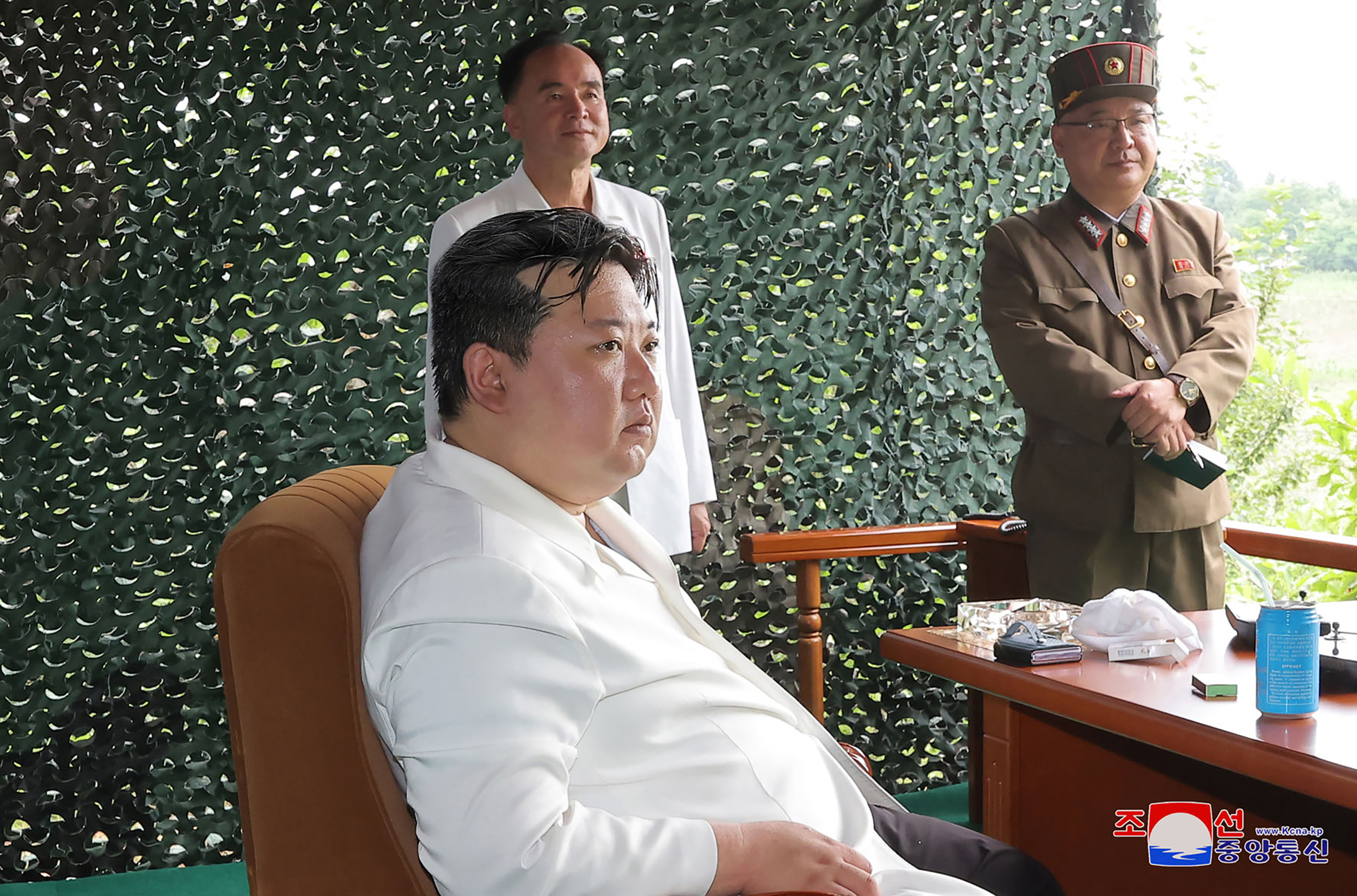 Kim Jong Un looking pensive as he sits in a chair ahead of the launch. He's in a camouflage hut, and senior military officials are behind him
