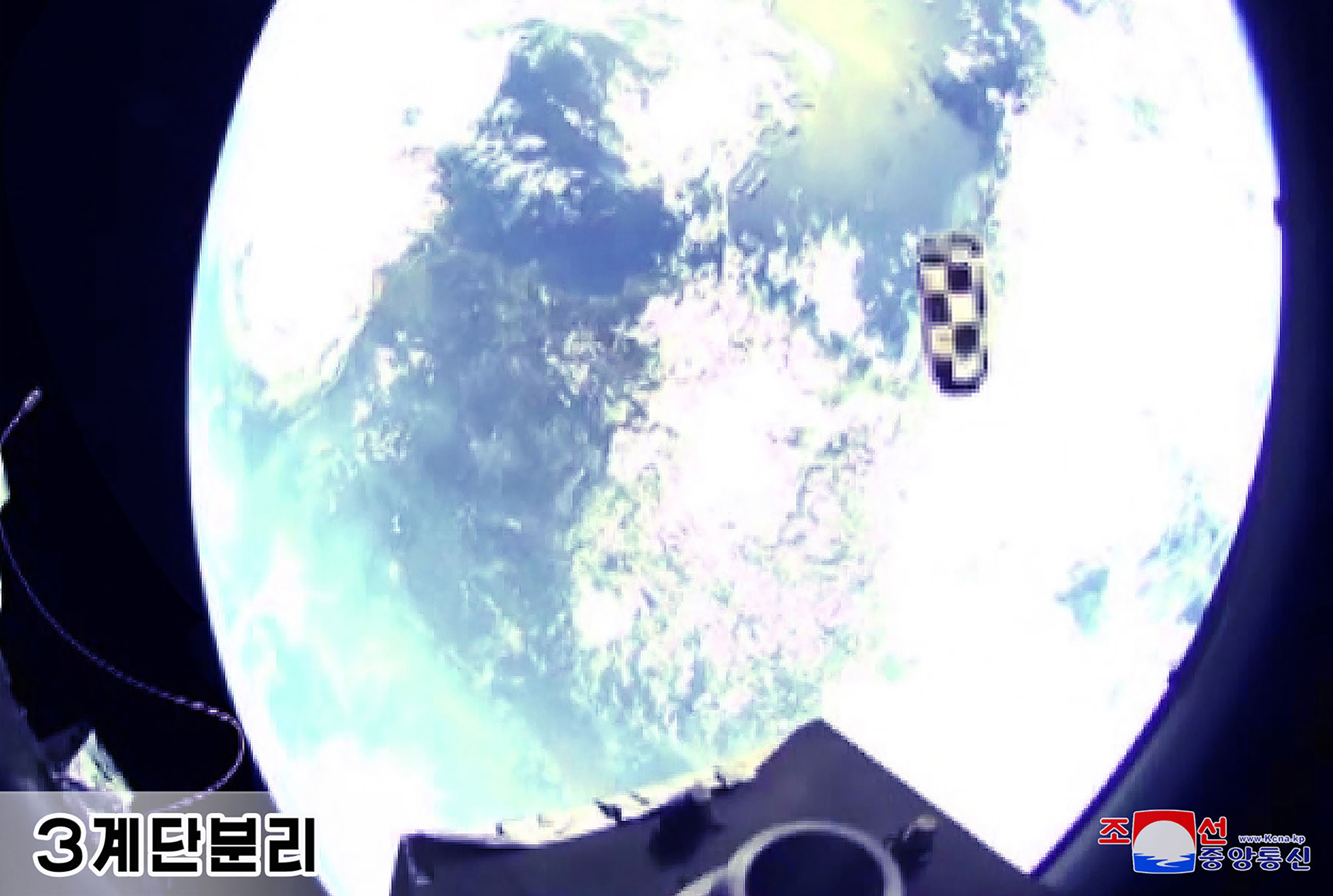 An image of the 'third stage' separation of the Hwasong-18. There is a small black and white cylindrical object to the right of the screen., and what appears to be Earth behind.