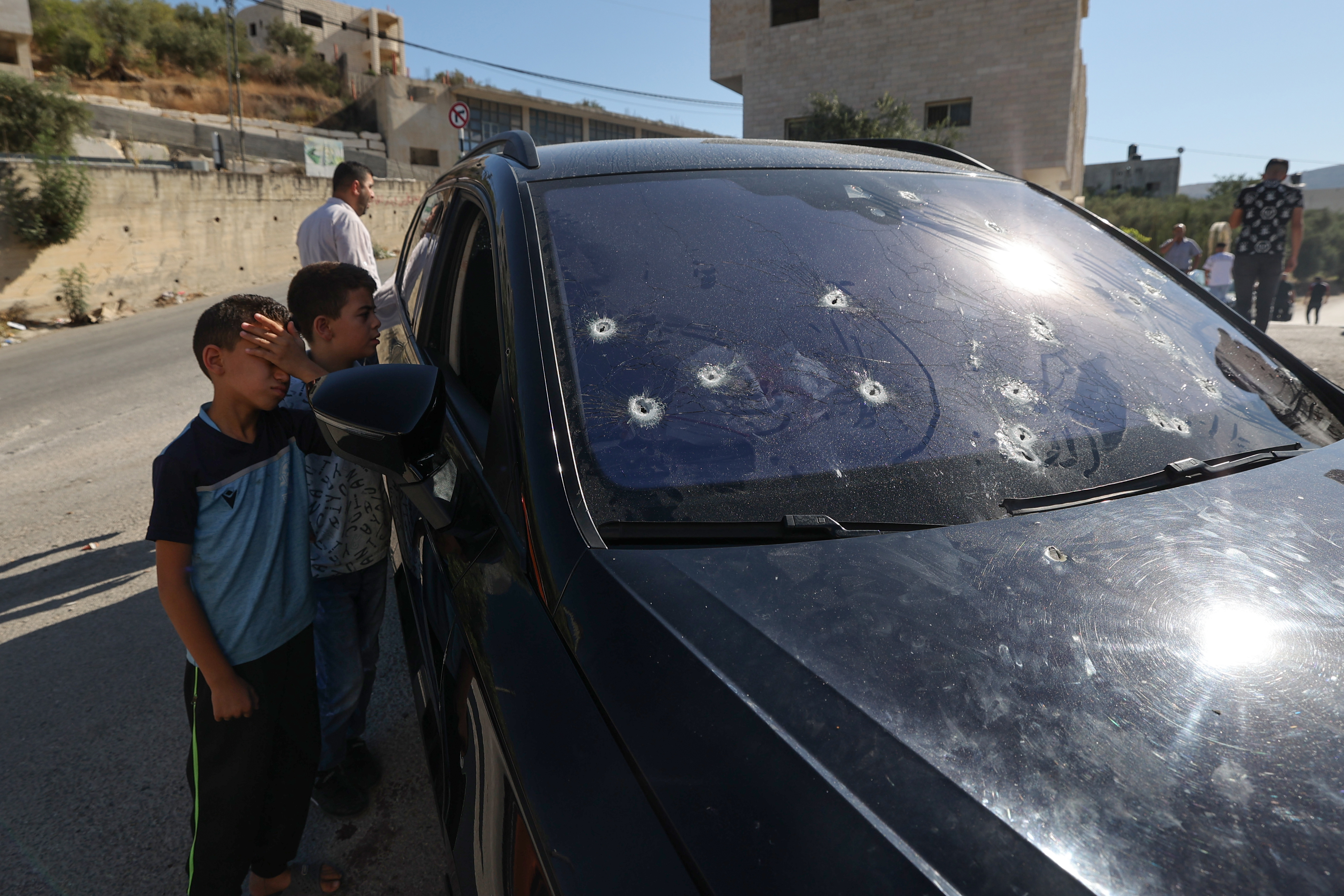Children stand next to a bullet-ridden car in which a Palestinian was killed