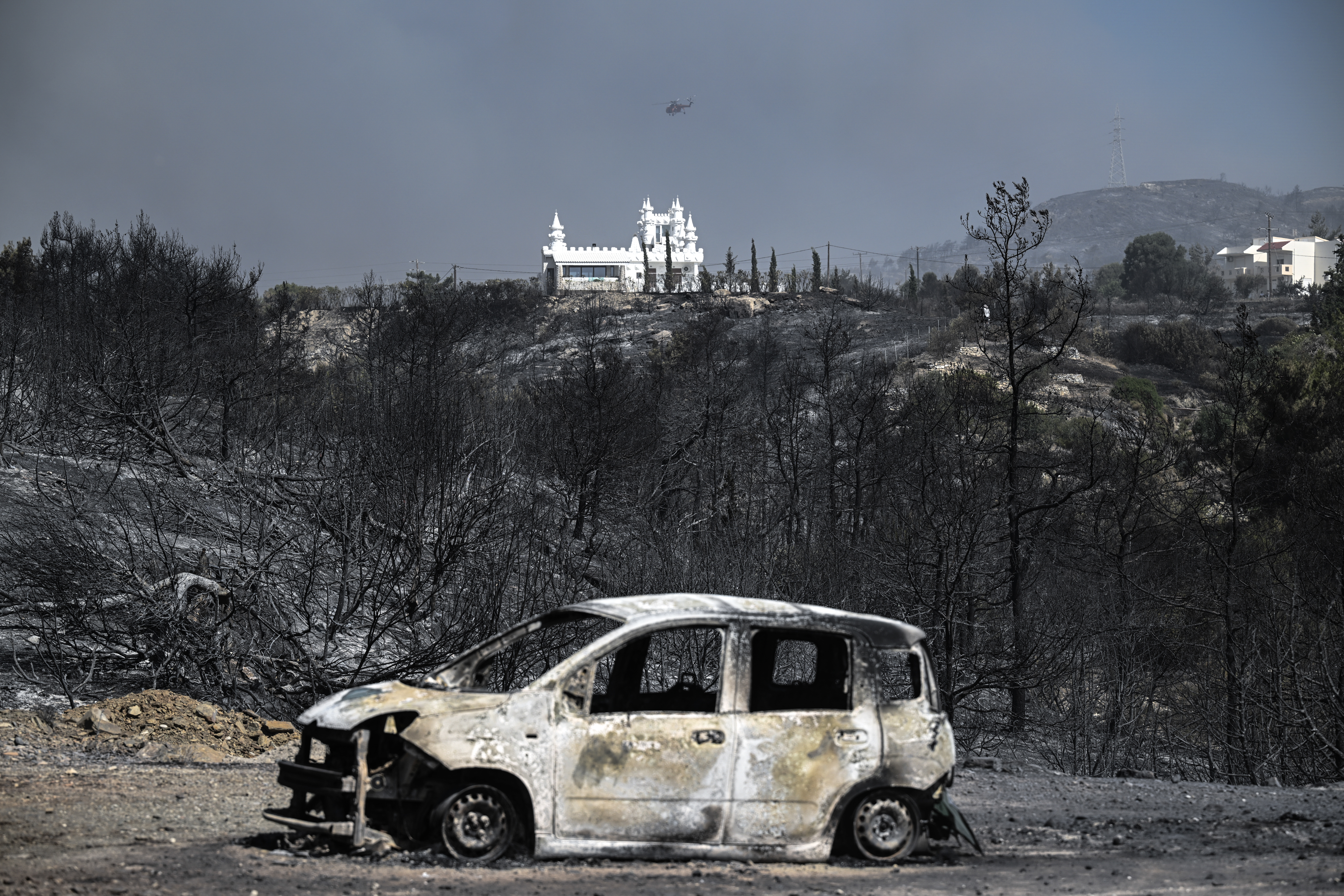 A burnt car sits in foreground of a charred area after a fire near the village of Kiotari, on the Greek island of Rhodes