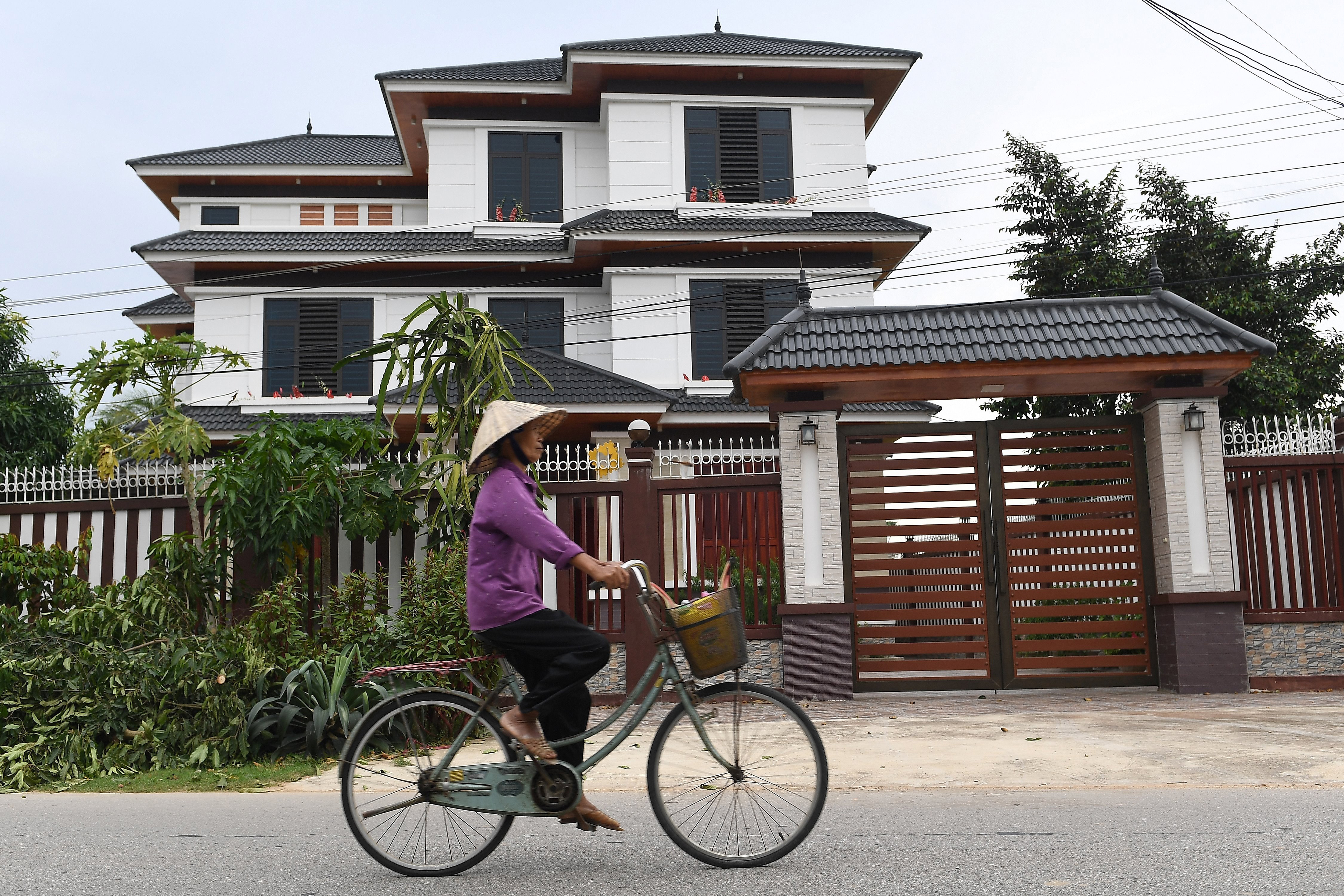 This photograph taken on October 10, 2020 shows a woman cycling past a new residential villa in a village in Vietnam's Nghe An province. - Four men are currently on trial in London over the deaths of 39 Vietnamese men and women who suffocated in a truck in Britain a year ago and they face various charges including manslaughter and conspiracy to smuggle people. (Photo by Nhac NGUYEN / AFP) / TO GO WITH Vietnam-Britain-migration, FOCUS by Tran Thi Minh Ha