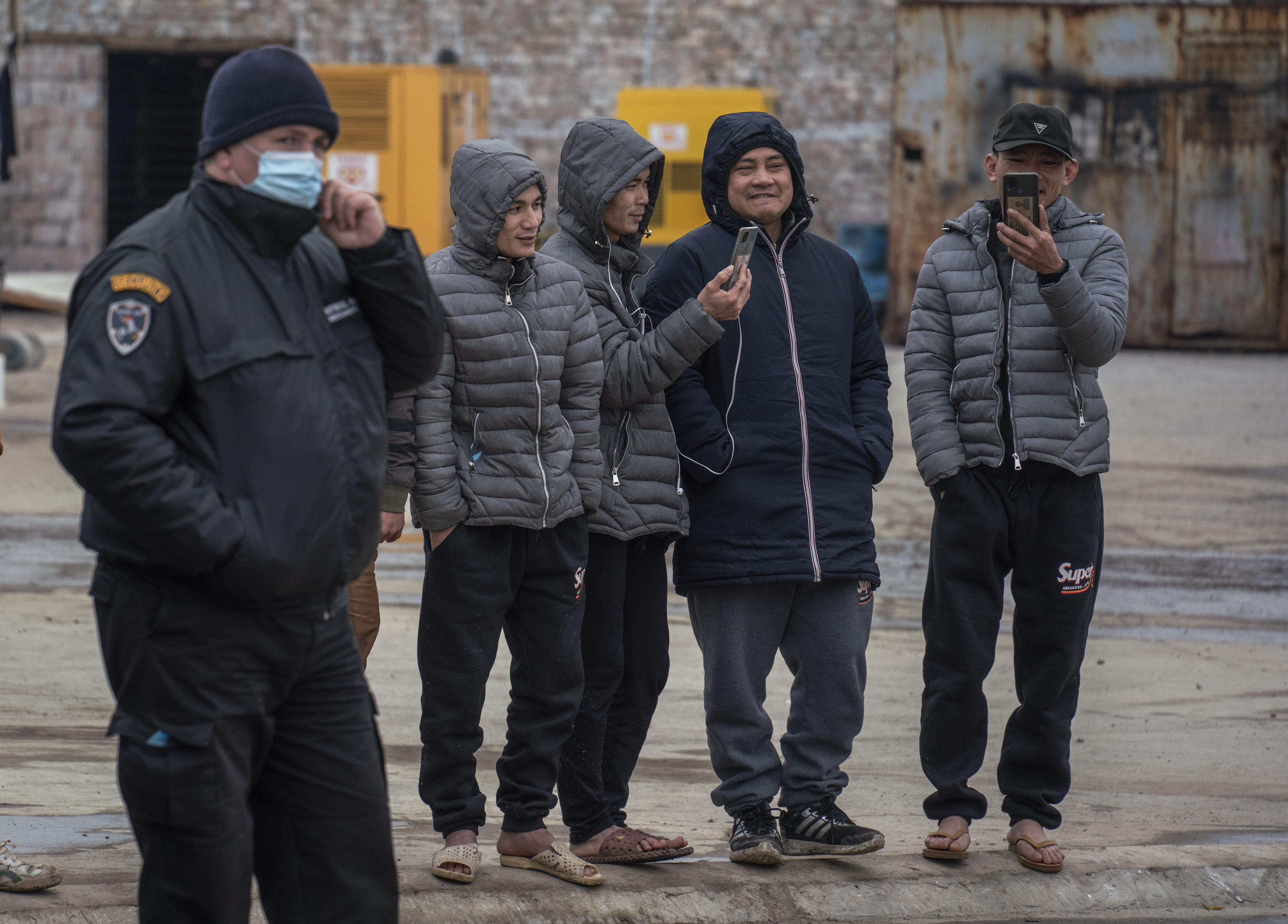Vietnamese workers look at their mobile phones as they hold a protest to call for better conditionson at the construction site of Chinese tyre factory Linglong near Zrenjanin, on November, 19 2021. - Some 500 Vietnamese workers went on strike last week, claiming they were unable to leave the company after being placed without heating, electricity and drinking water in dilapidated quarters of an abandoned factory. This was the third time in less than six months Vietnamese workers went on strike according to the report, first two were because of lack of food and unpaid salaries. (Photo by OLIVER BUNIC / AFP)
