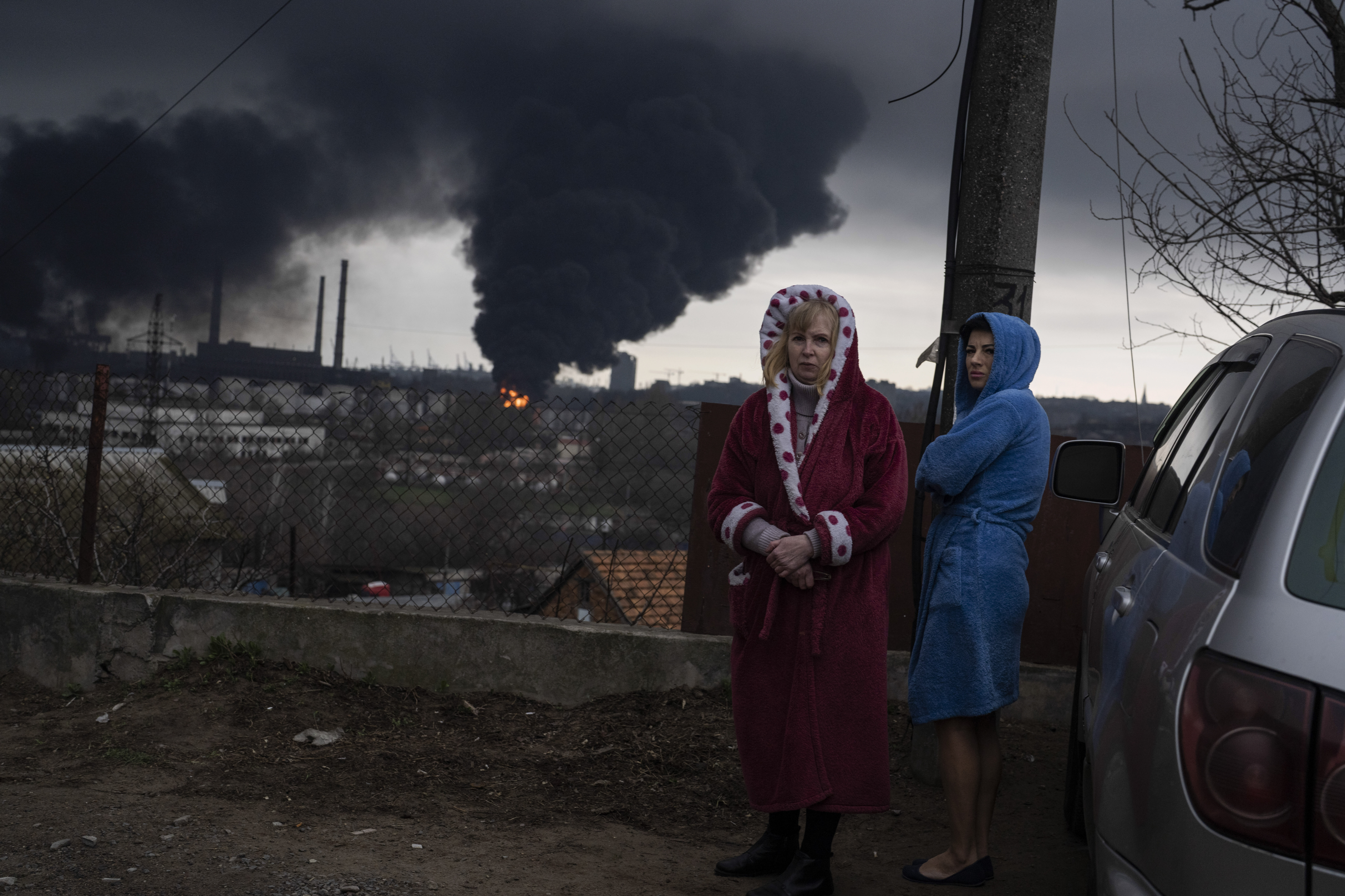 Women stand next to a car as smoke rises in the air in the background after shelling in Odesa,