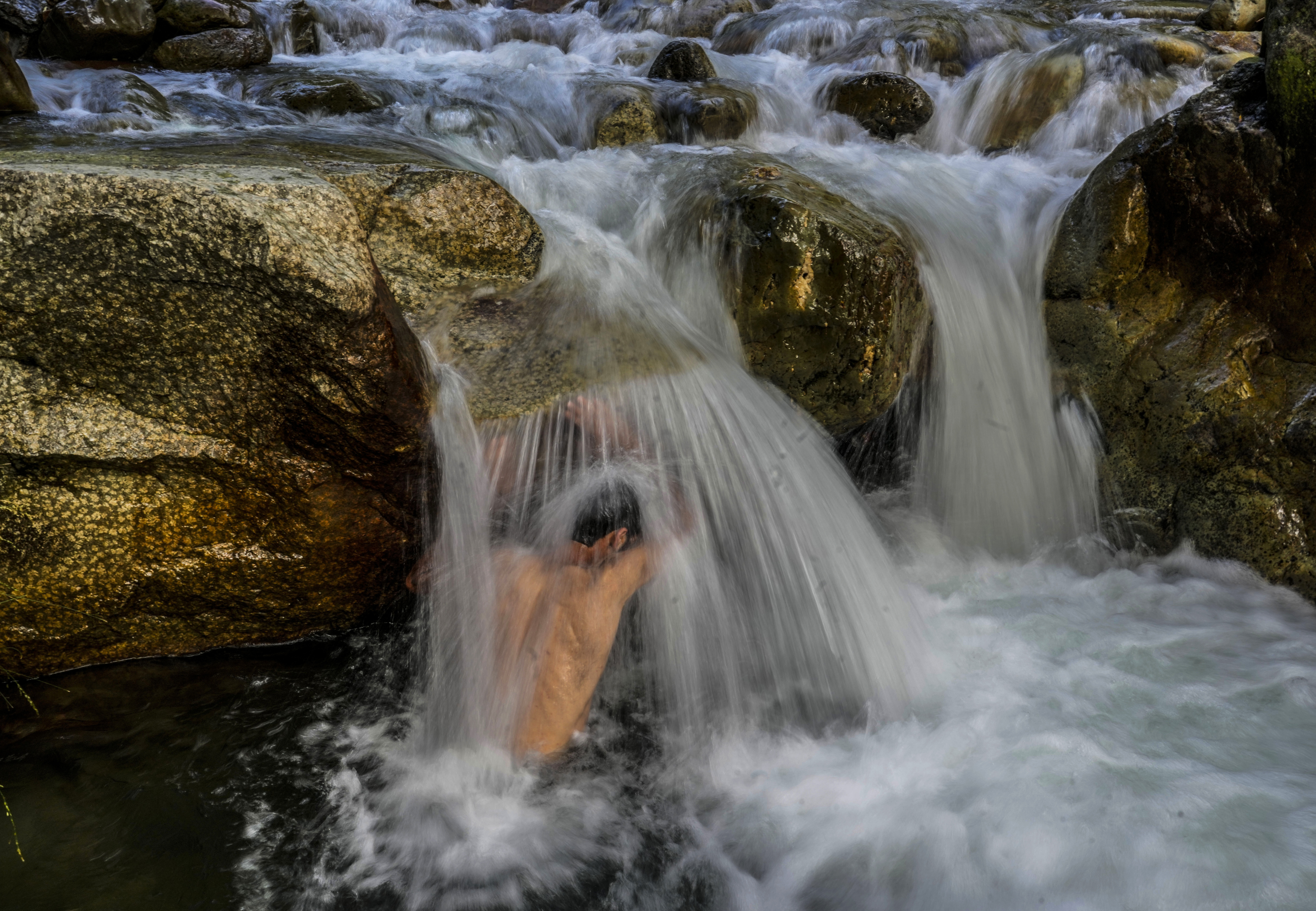 A Kashmiri man cools off at a stream on a hot summer day