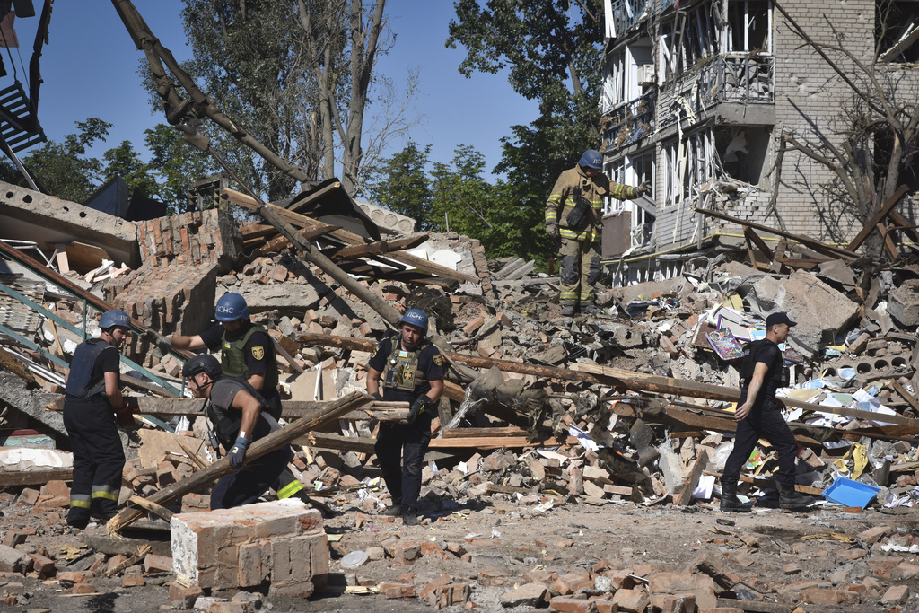 Rescue teams work at the scene of a Russian missile attack on the Ukrainian town of Orikhiv. They are walking across piles of rubble with a damaged block of flats behind.