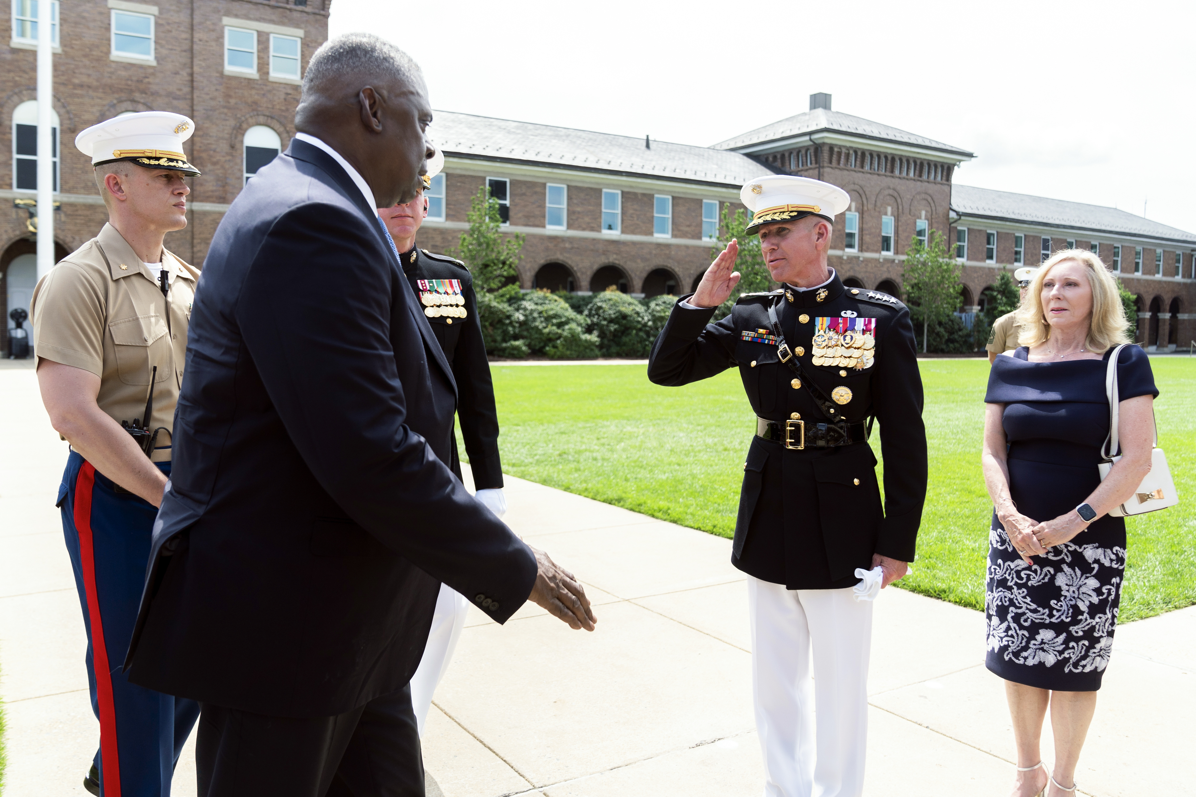 A man in a dark suit walks toward a marine, who salutes him.