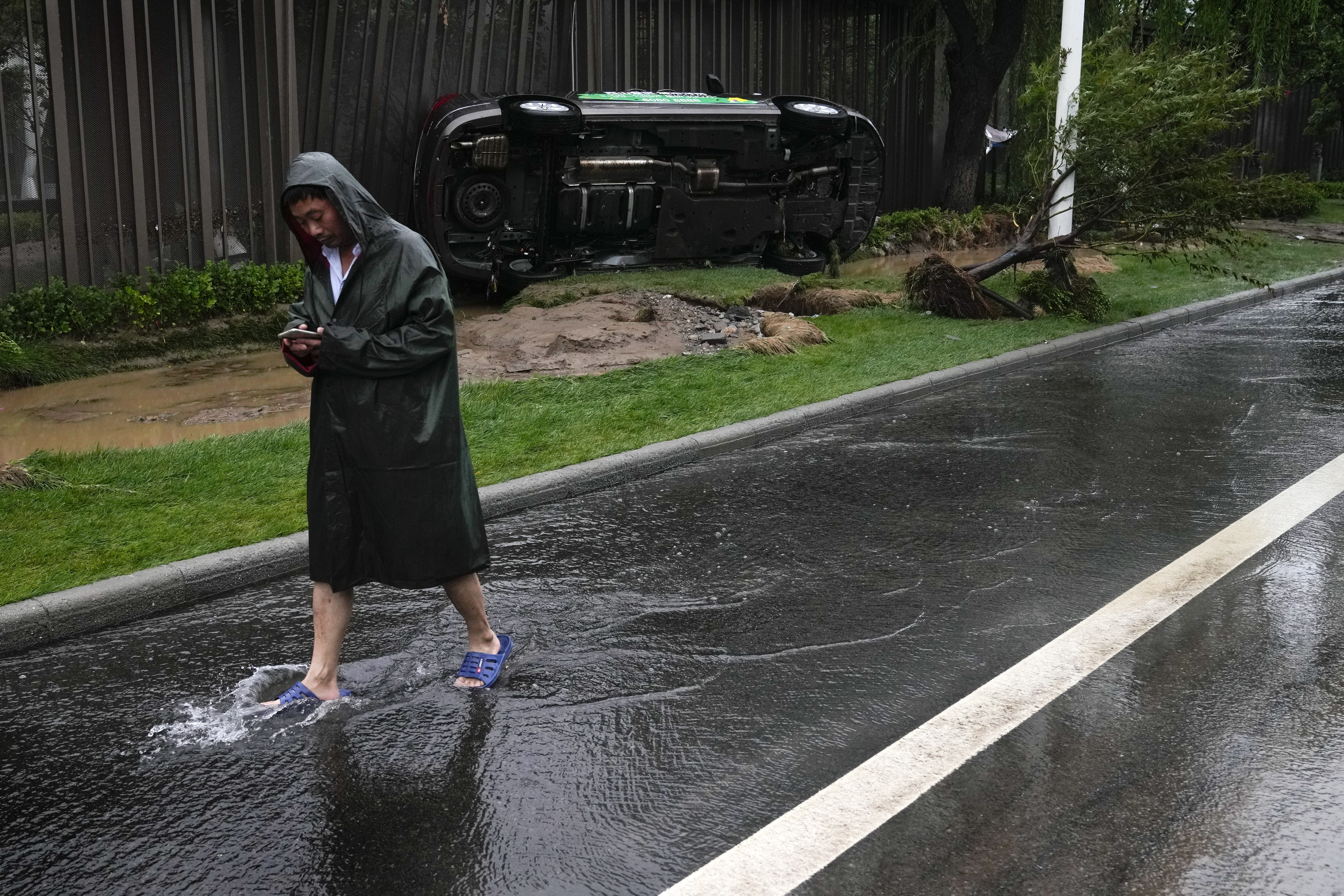 A man walks by a damaged vehicle which swept away by flood water