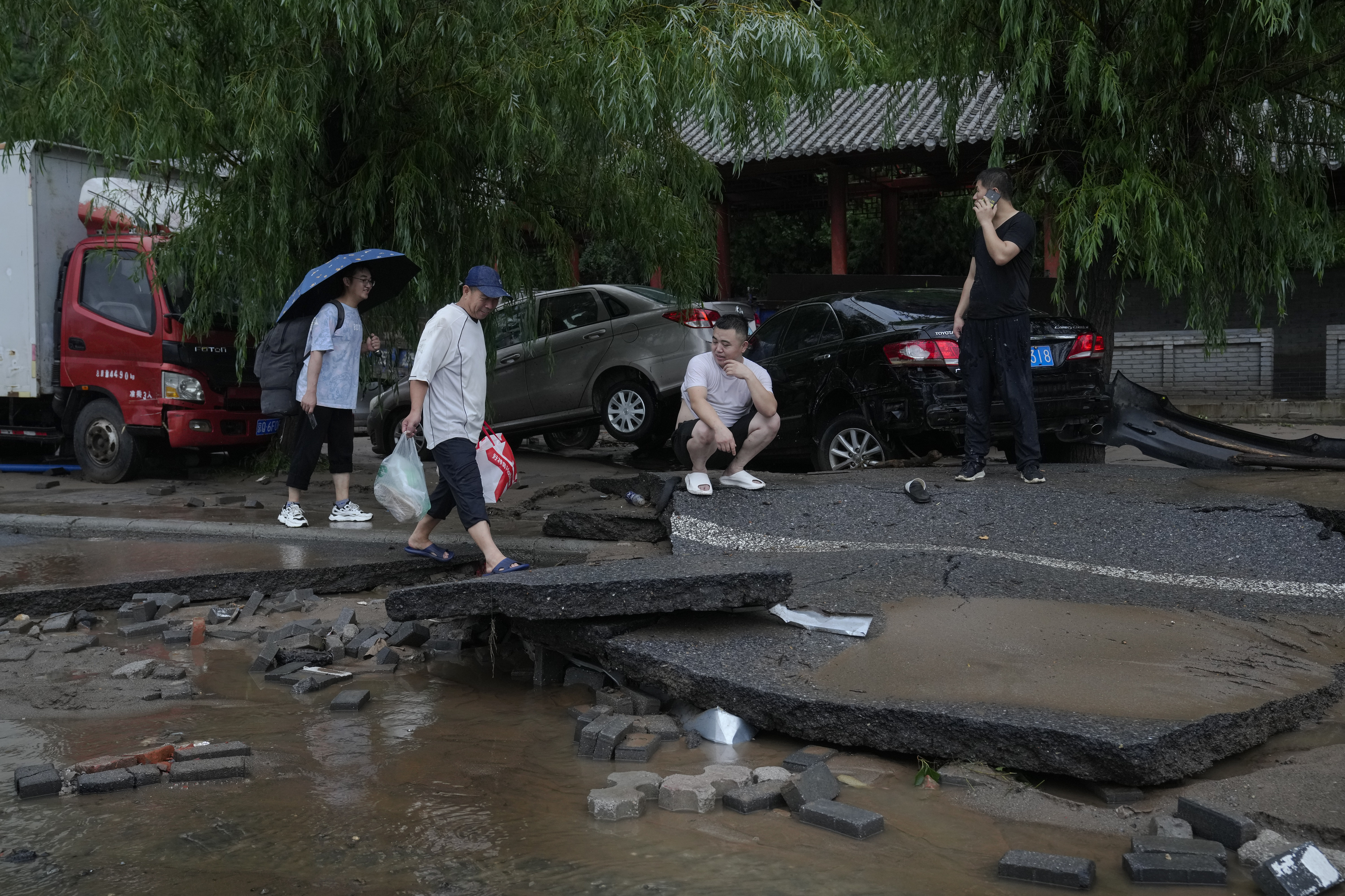 People walk along a damaged road and vehicles swept by flood water