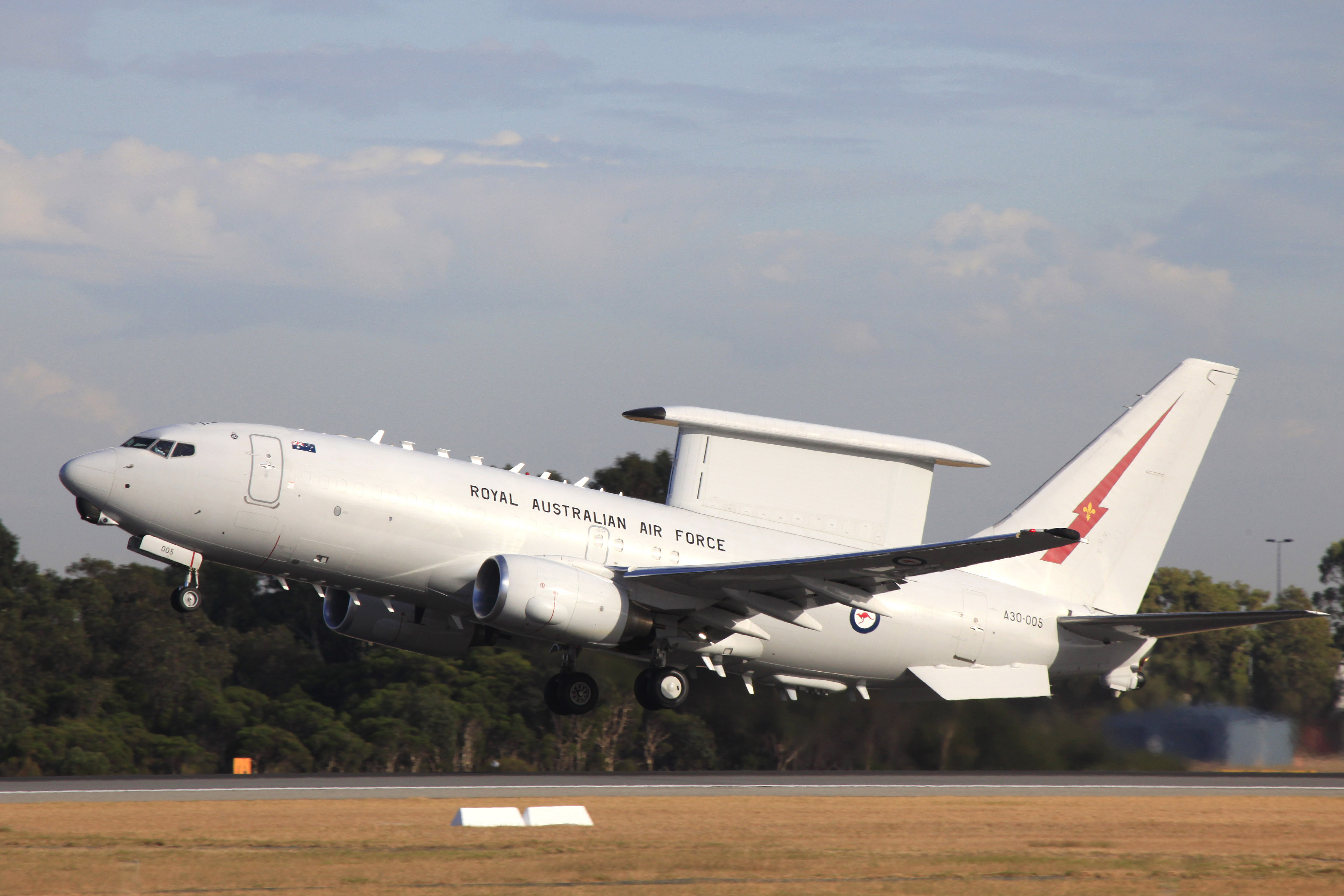 An Australian Air Force Wedgetail taking off. The plan is white and has a large rectangular surveillance unit on top. There's a red stripe on the tail.