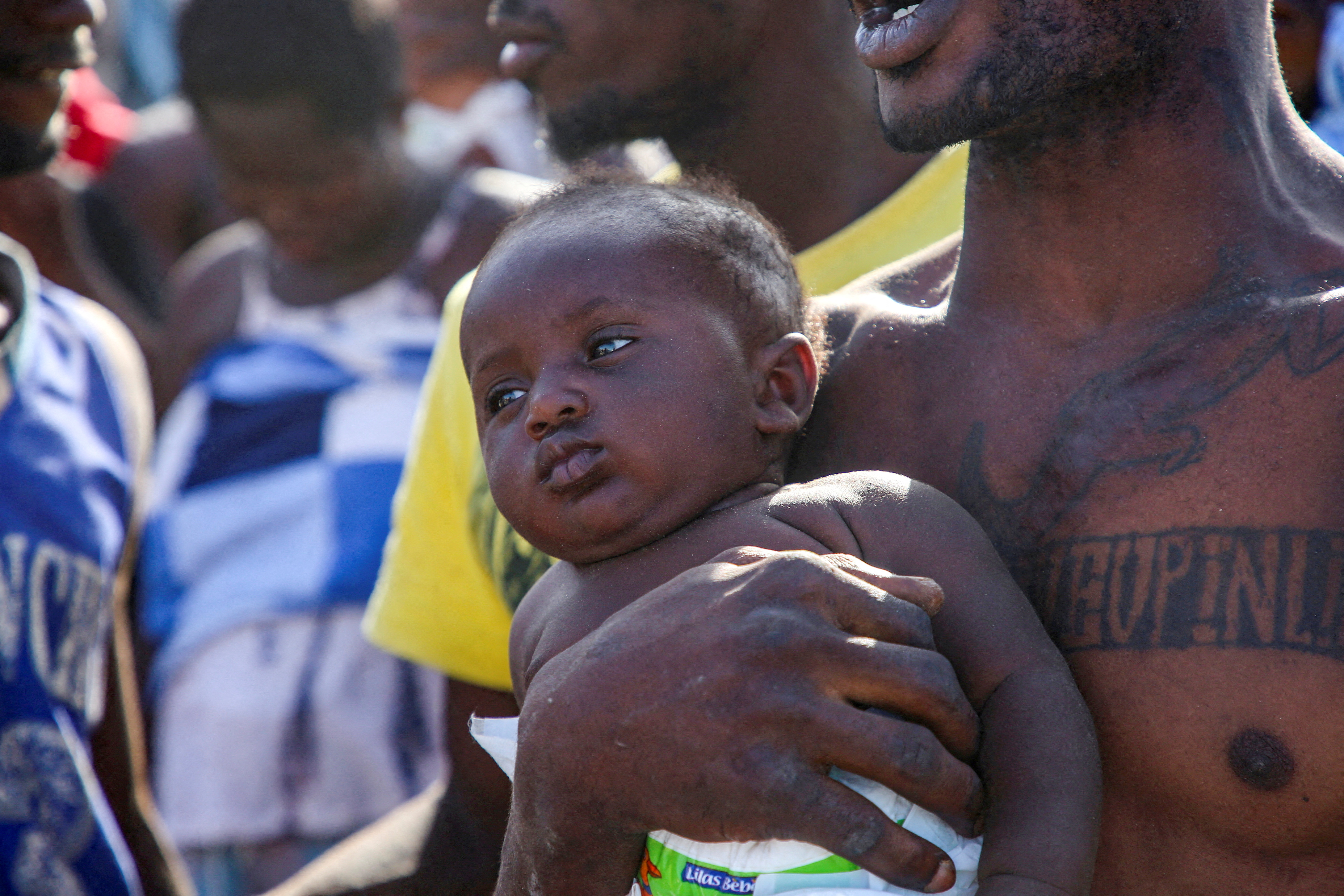 A migrant from Africa carries a child next to the seashore, at the Libyan-Tunisian border in Ras Ajdir, Libya