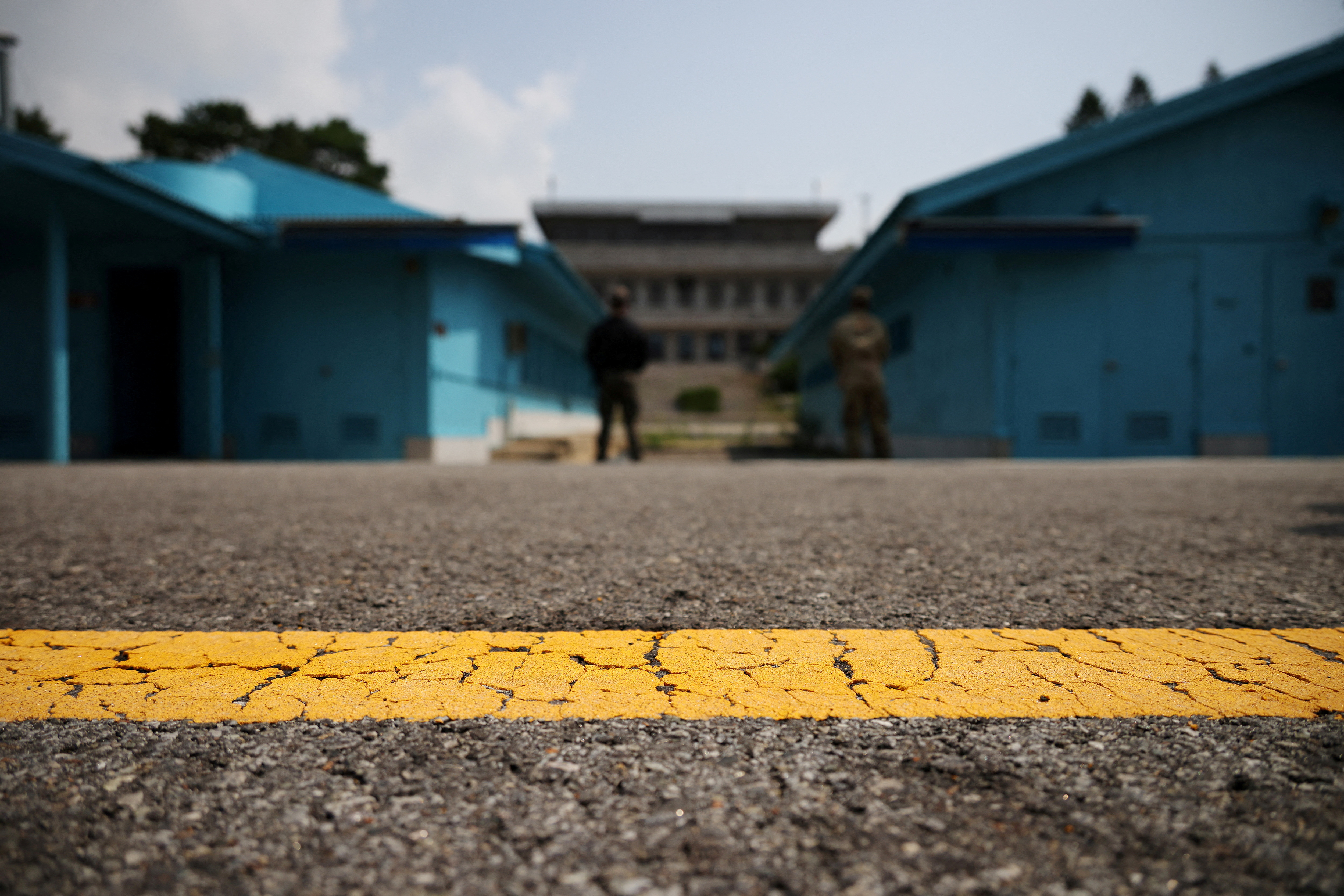 A view of the Joint Security Area at the truce village of Panmunjom. There is a yellow line painted on the road in front, and low-rise blue buildings on either side.