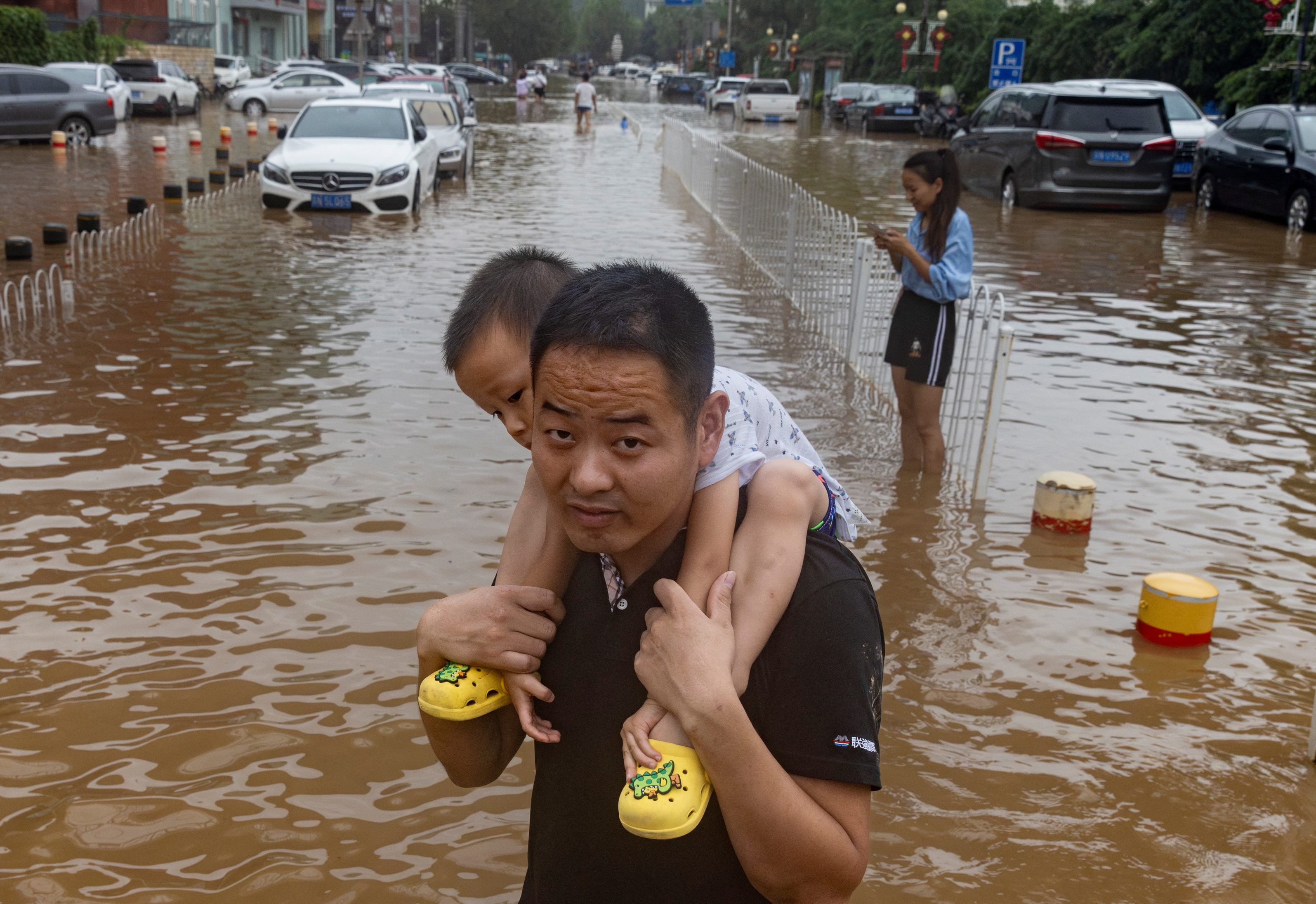 A man carries a child through a flooded street in a neighbourhood where days of heavy rain from remnants of Typhoon Doksuri have caused heavy damage in Beijing