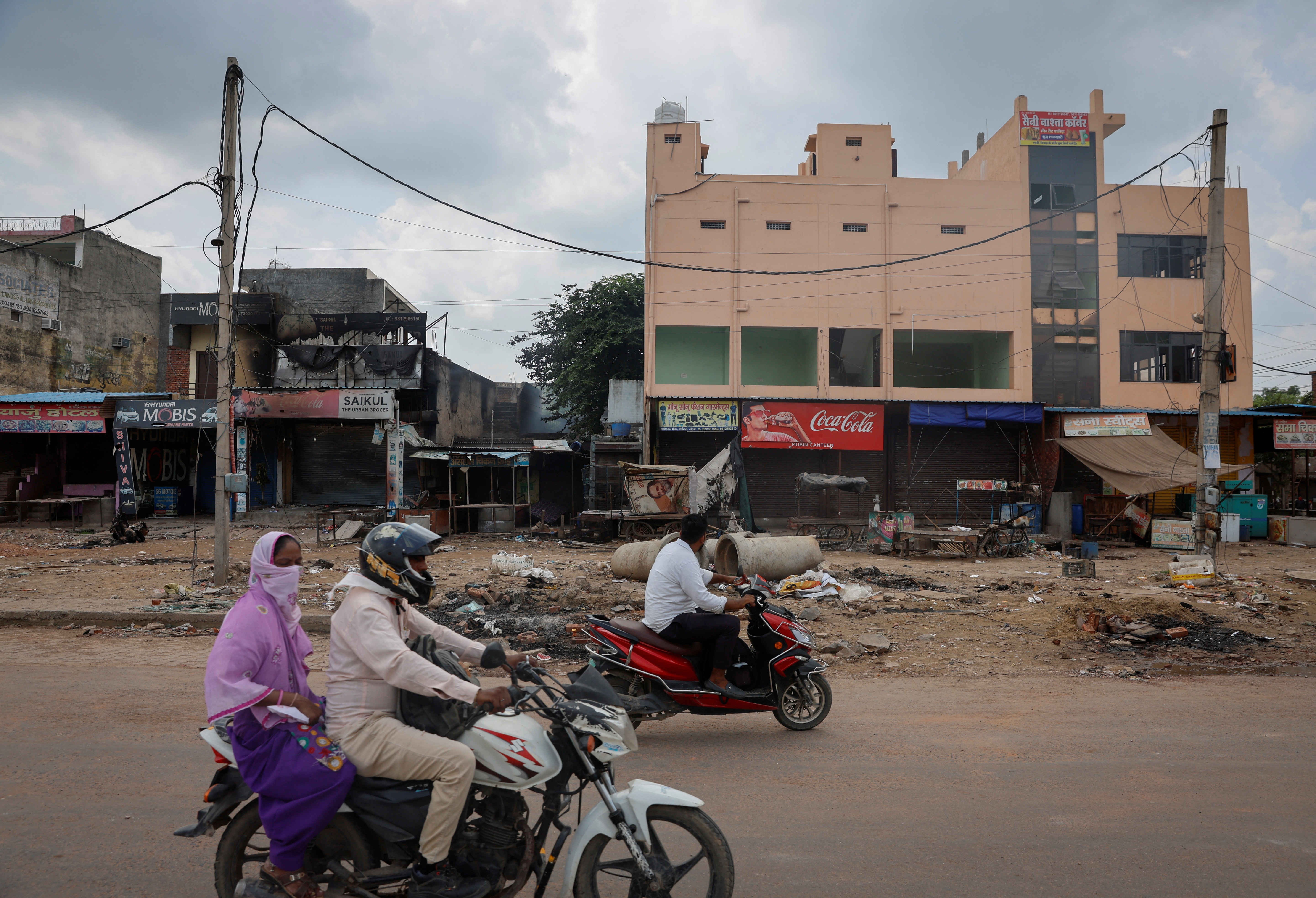 People ride past the burnt shops following clashes between Hindus and Muslims in Gurugram district