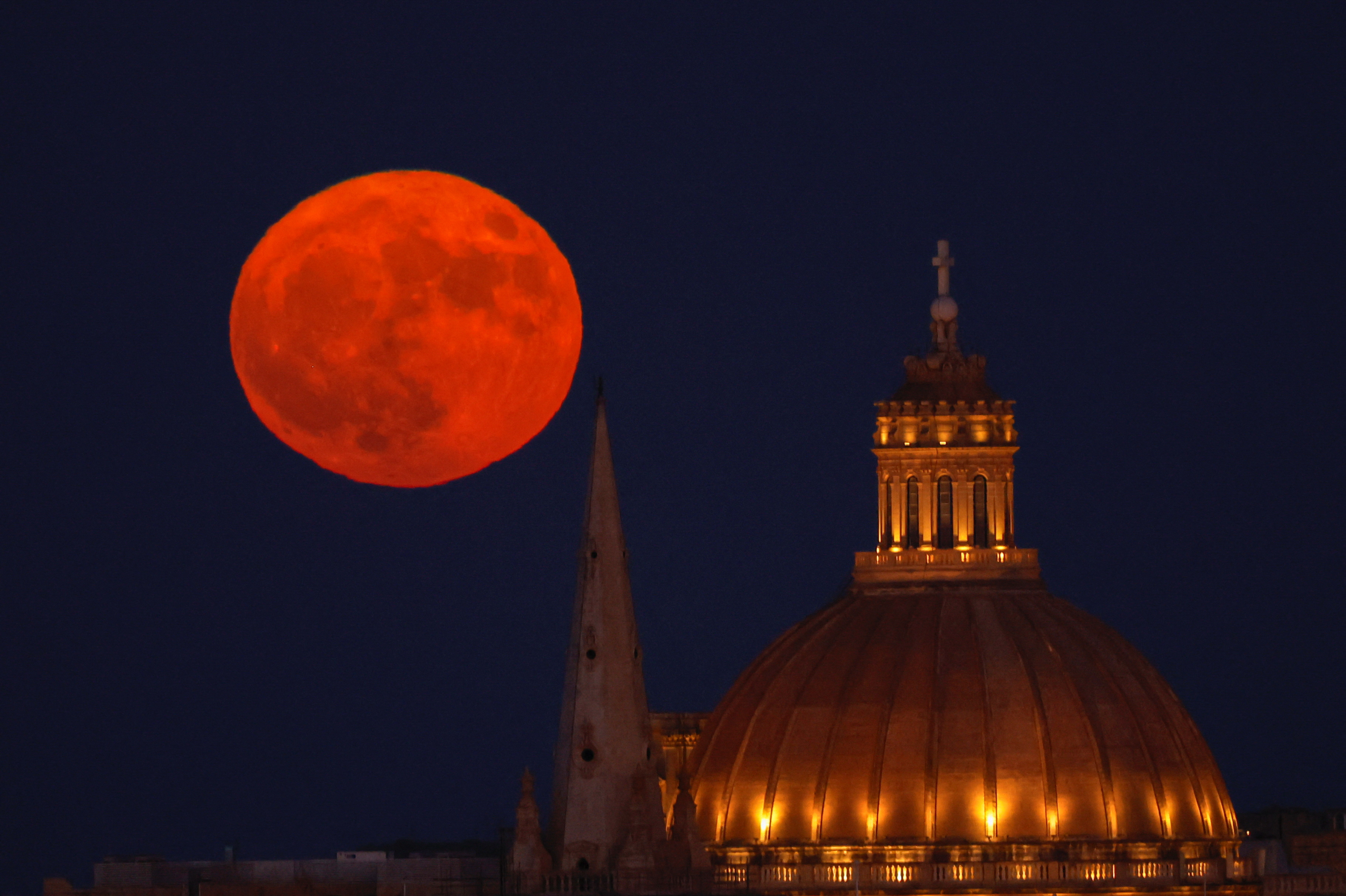 The Sturgeon Supermoon rises behind the steeple of St Paul's Anglican Pro-Cathedral and the dome of the Basilica of Our Lady of Mount Carmel in Valletta