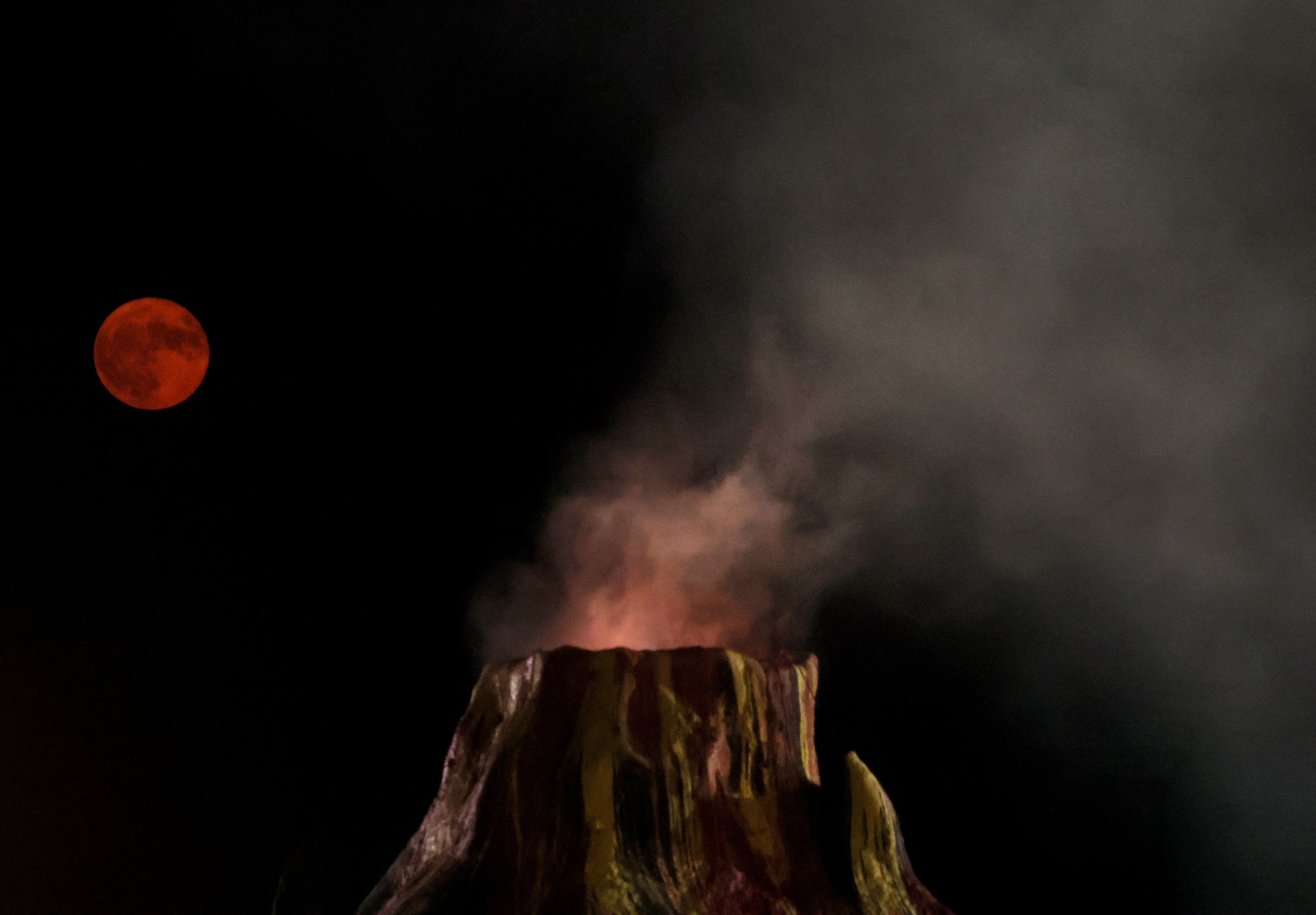 The full Sturgeon Moon rises over the smoking Fire Mountain volcano from the mini golf course of Midway Speedway Park in Rehoboth Beach, Delaware