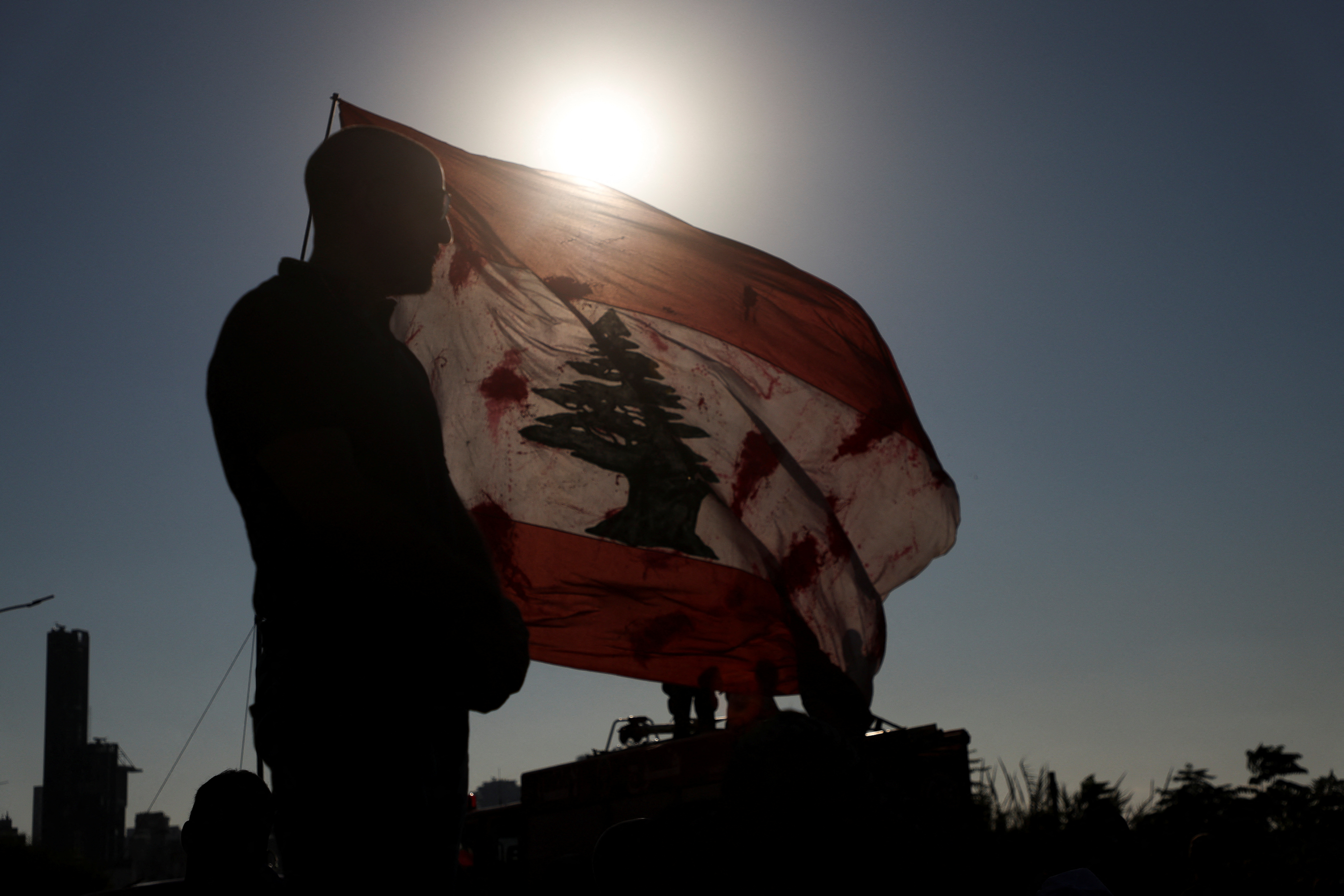A man stands near a Lebanese flag stained in red paint, mimicking blood, during a march as Lebanon marks the three-year anniversary of August 4 Beirut port explosion