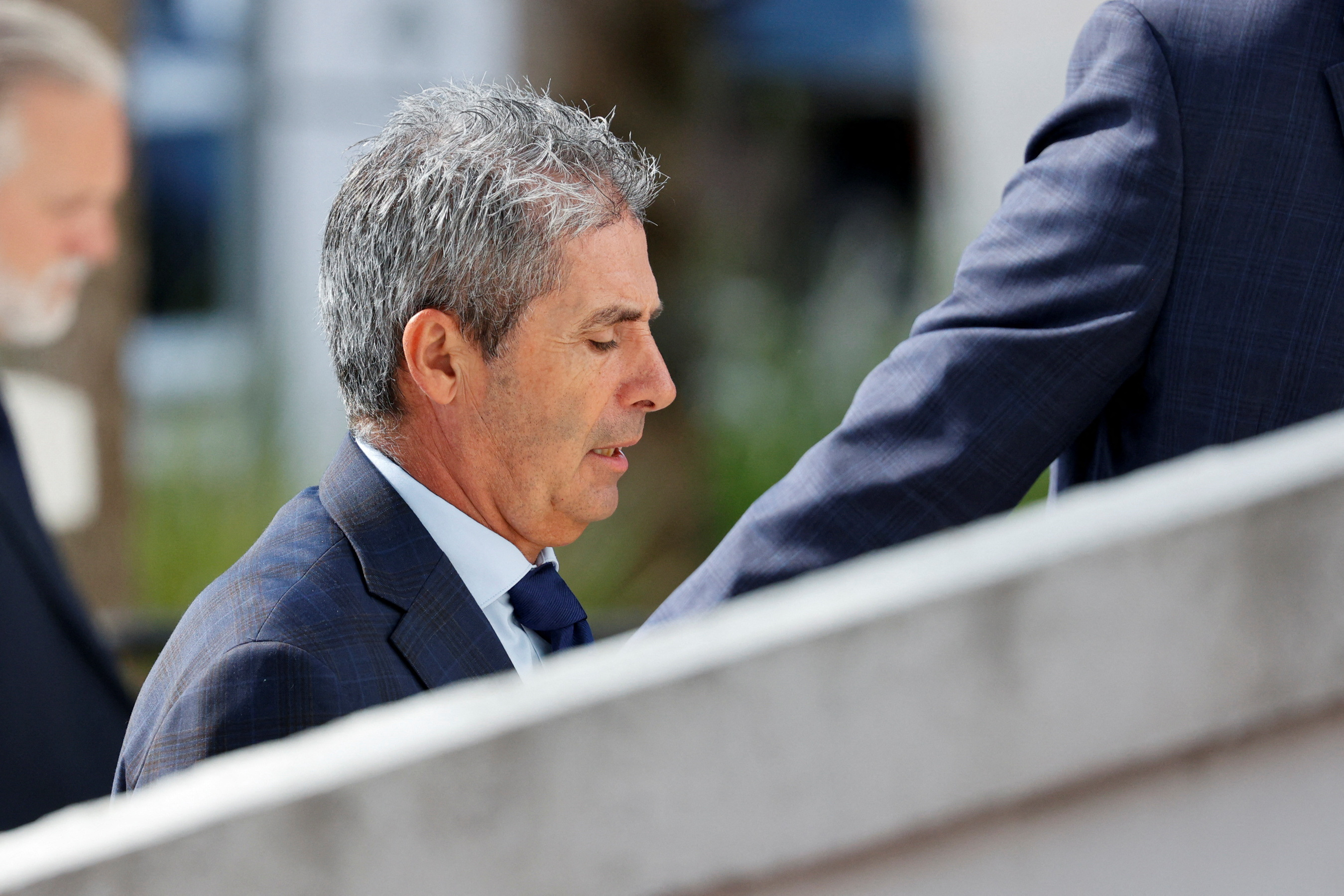 A close-up of a man in a dark suit and tie, as he walks up the steps to a courthouse.