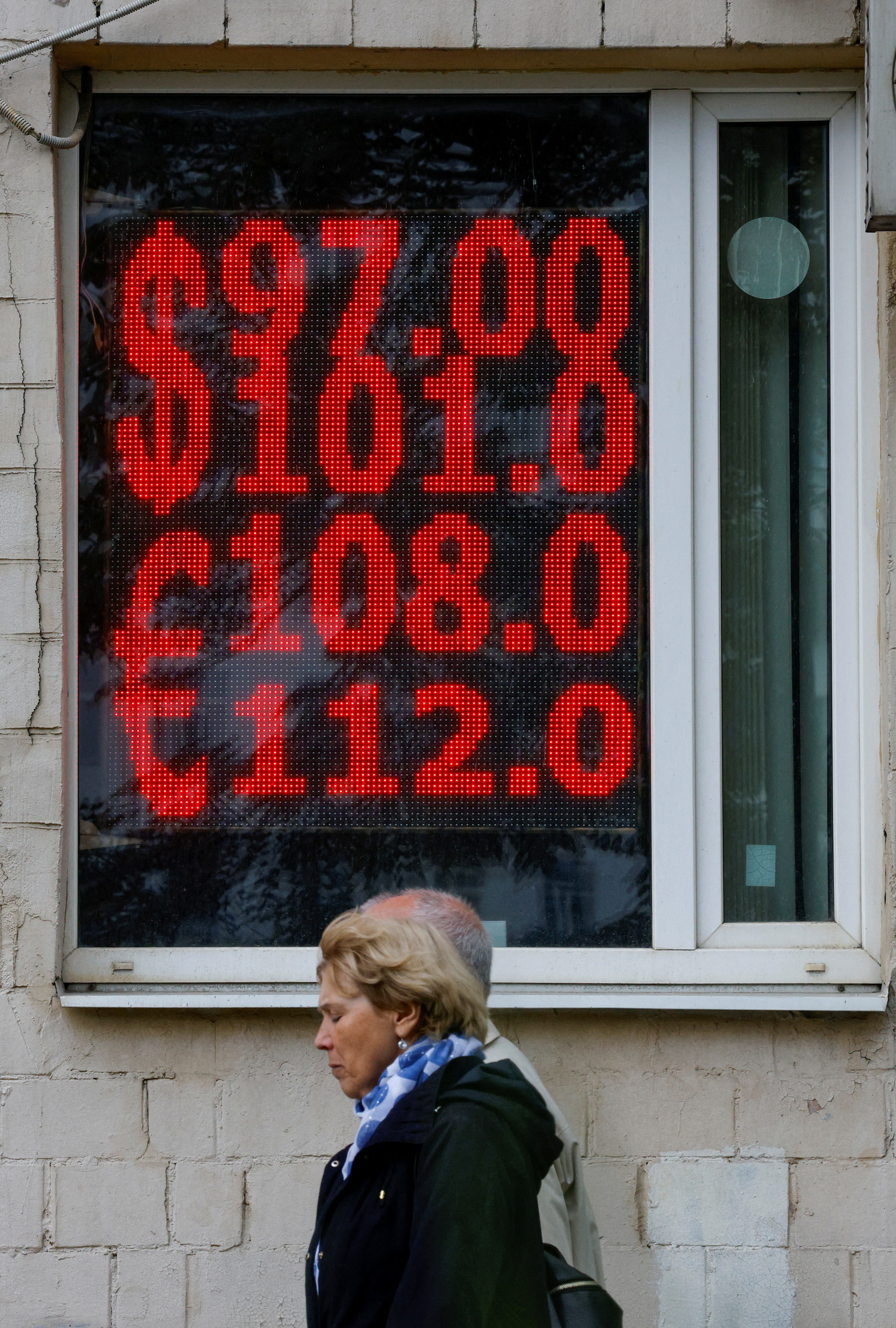 People walk past an electronic board showing currency exchange rates of the U.S. dollar and euro against Russian rouble in a street in Moscow