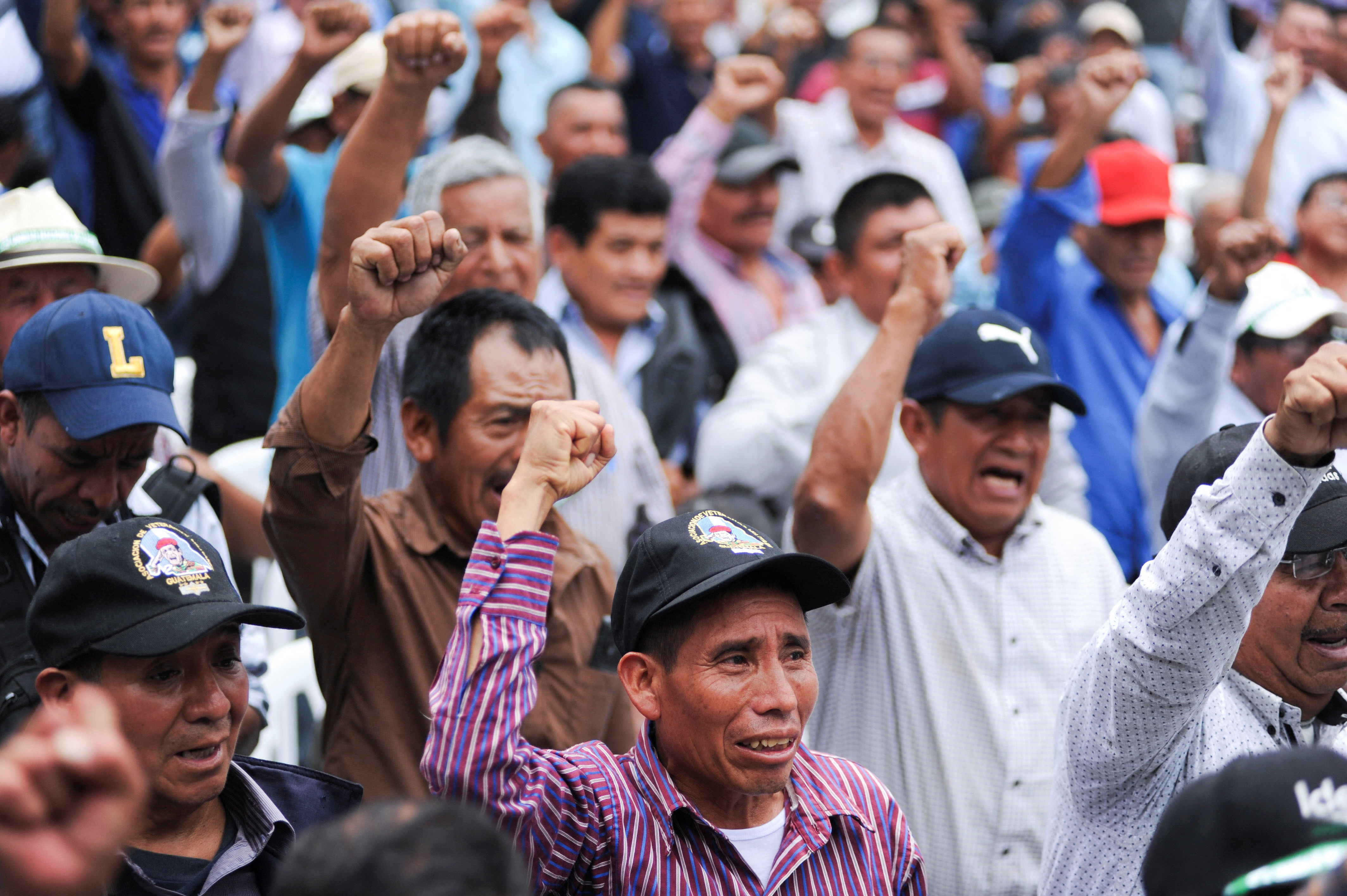 A large crowd of veterans, many wearing baseball caps and collared shirts, raise their fists as they attend a rally for Sandra Torres.