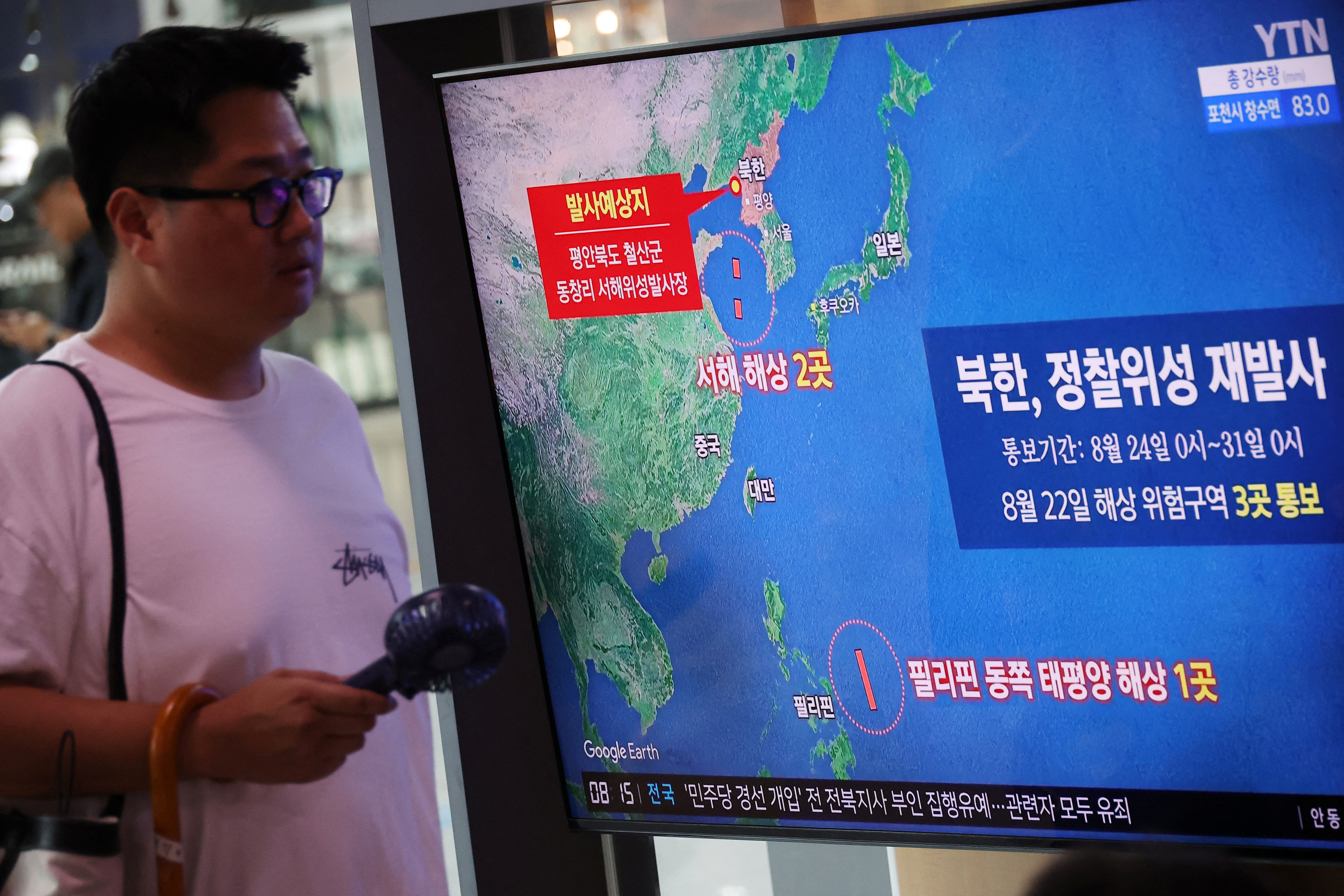 A man in Seoul walking past a large TV screen showing a map of North Korea's satellite launch.