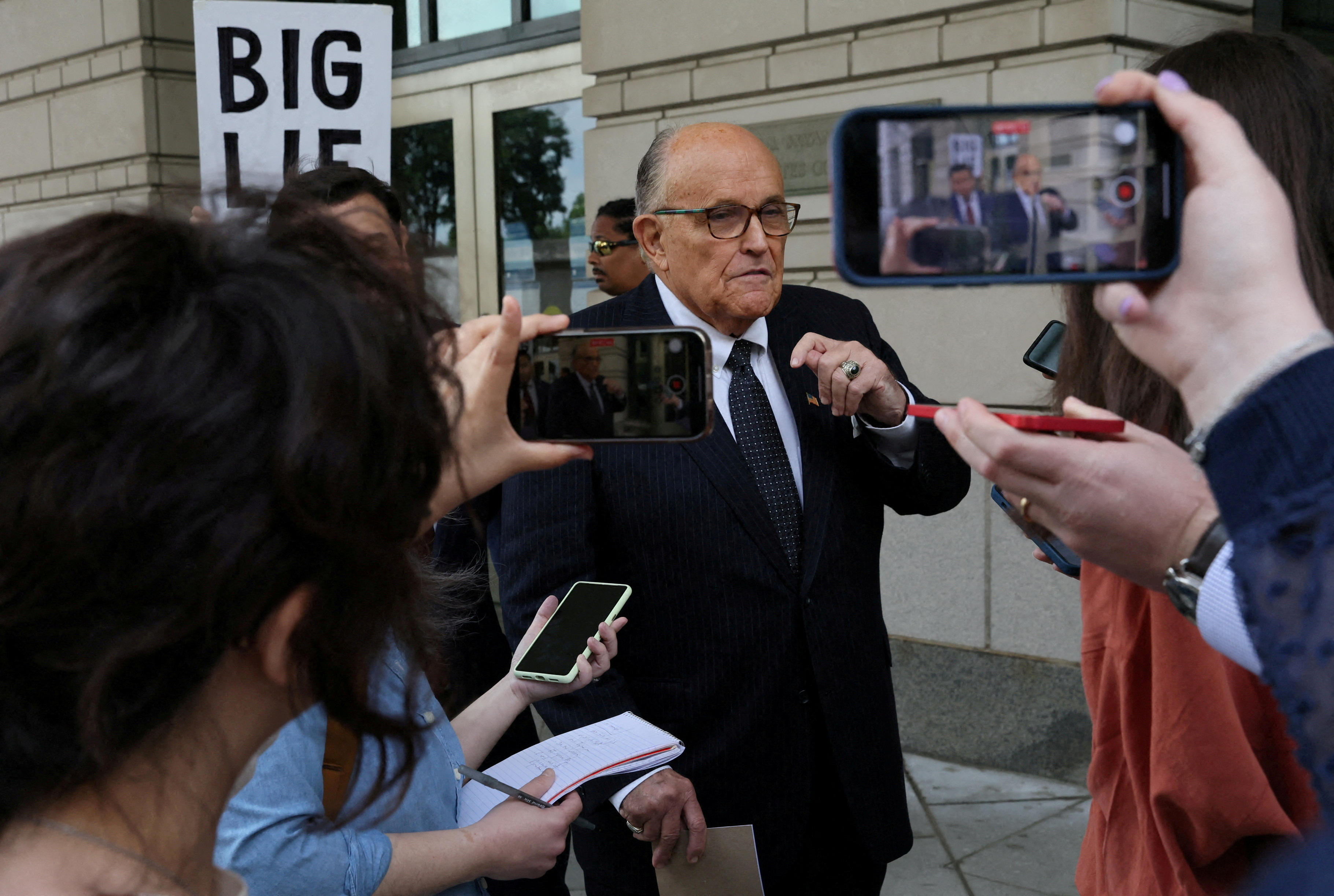 Onlookers and reporters point cellphones and microphones at Rudy Giuliani as he leaves a US district court.