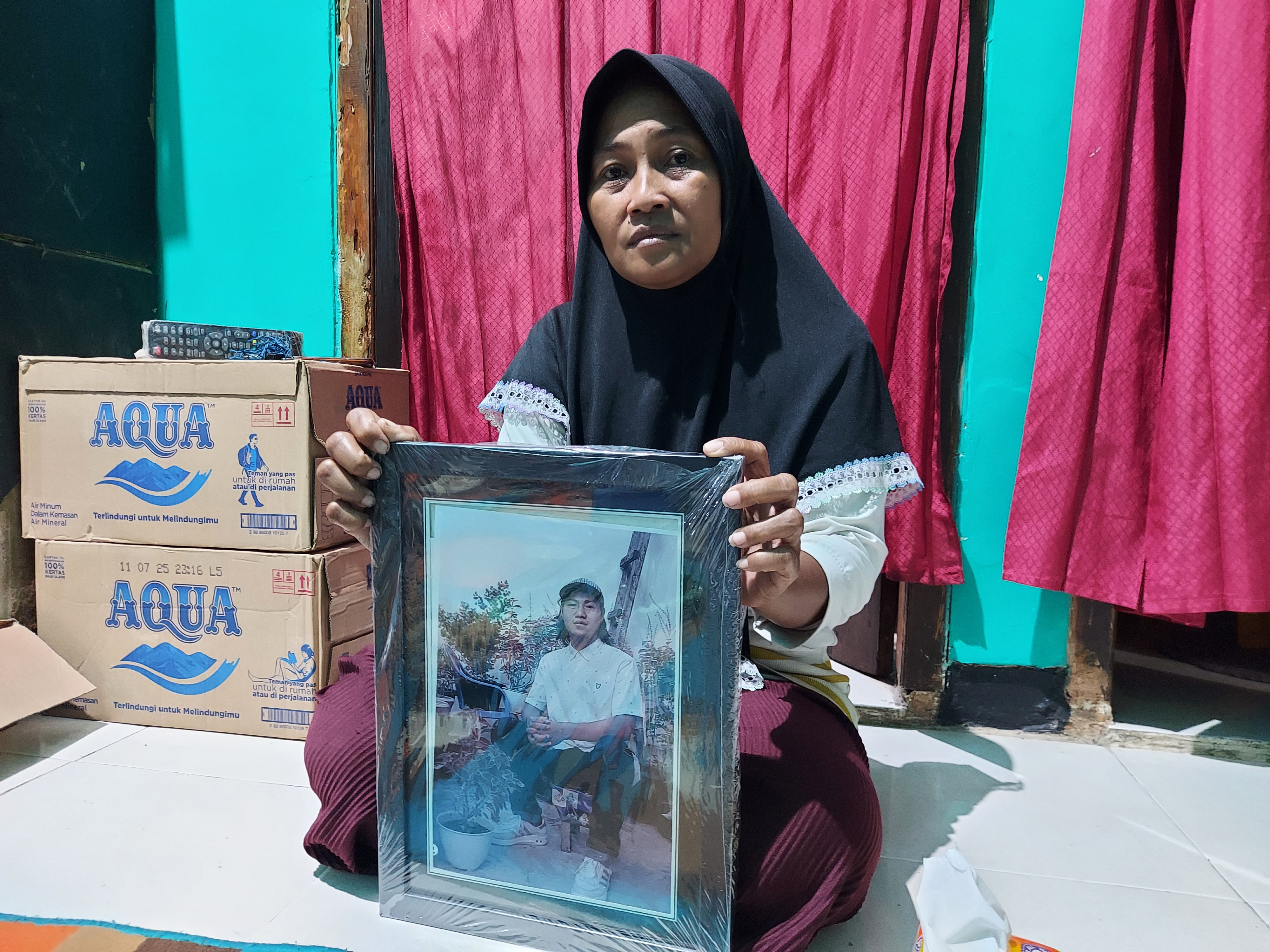 Rini Hanifa holds a picture of her son Agus. She is seated on the floor holding up the large framed photo