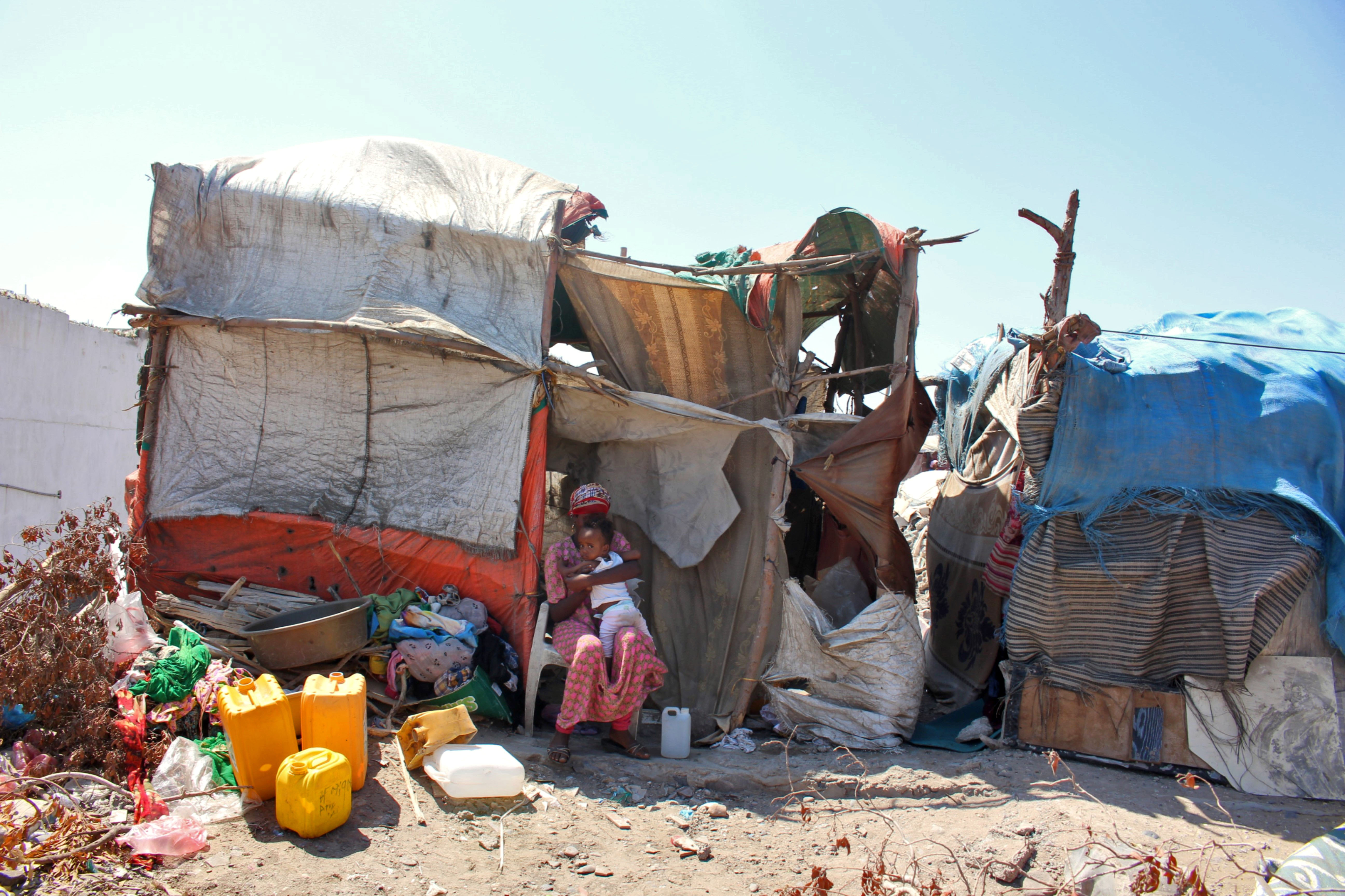 Ethiopian refugee woman holding a child in front of a makeshift shelter made with pieces of cloth and sticks