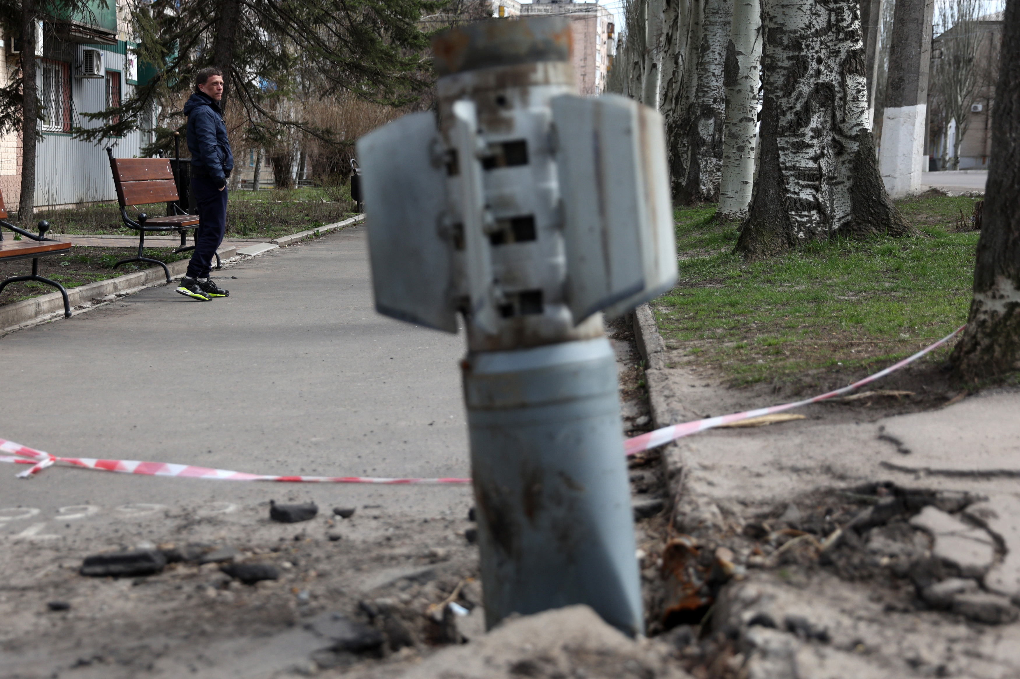A man walks past an unexploded tail section of a 300mm rocket which appear to contained cluster bombs launched from a BM-30 Smerch multiple rocket launcher embedded in the ground after shelling in Lysychansk, Lugansk region on April 11, 2022