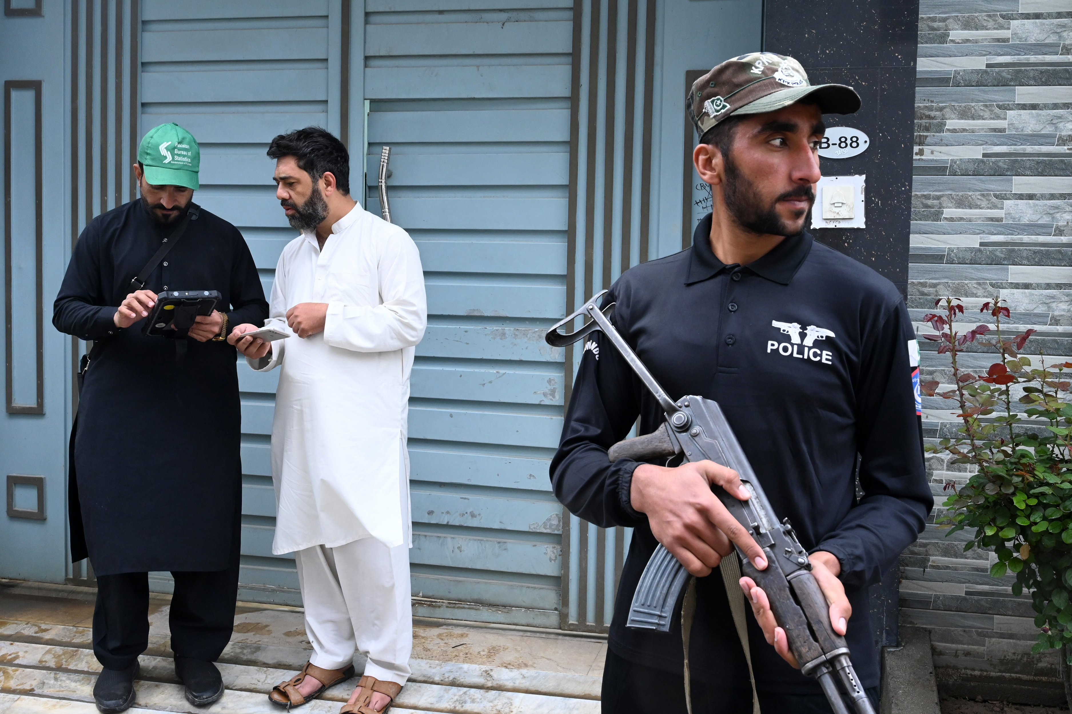 A security personnel (R) stands guard next to an official (L) from the Pakistan Bureau of Statistics using a digital device to collect information from residents during the first ever door-to-door digital national census in Peshawar, in Khyber Pakhtunkhwa province on March 25, 2023. (Photo by Abdul MAJEED / AFP)