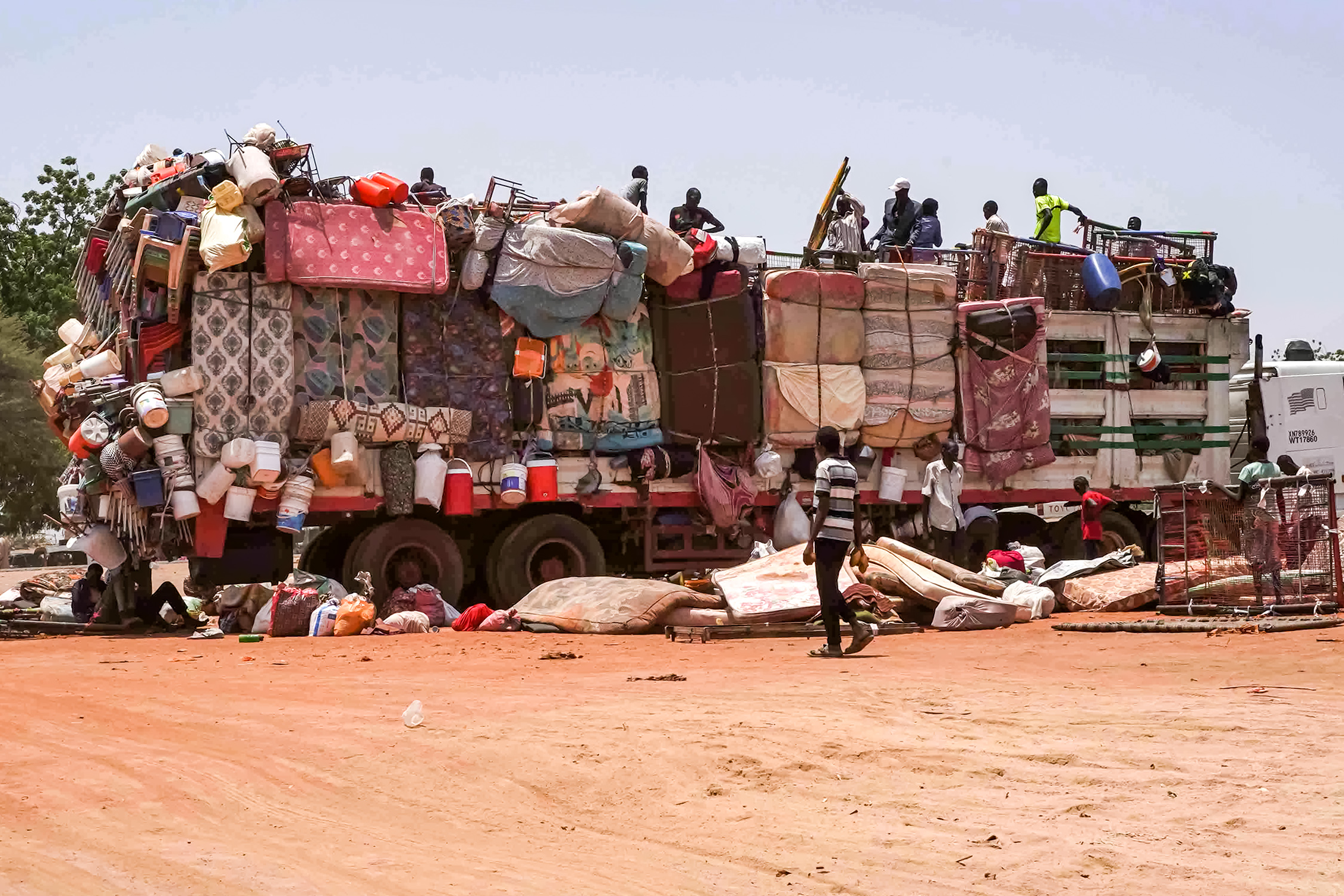 People sit atop a truck carrying mattresses, plastic chairs, and other pieces of furniture parked along the road connecting Sudan's capital to the city of Wad Madani in al-Jazirah state