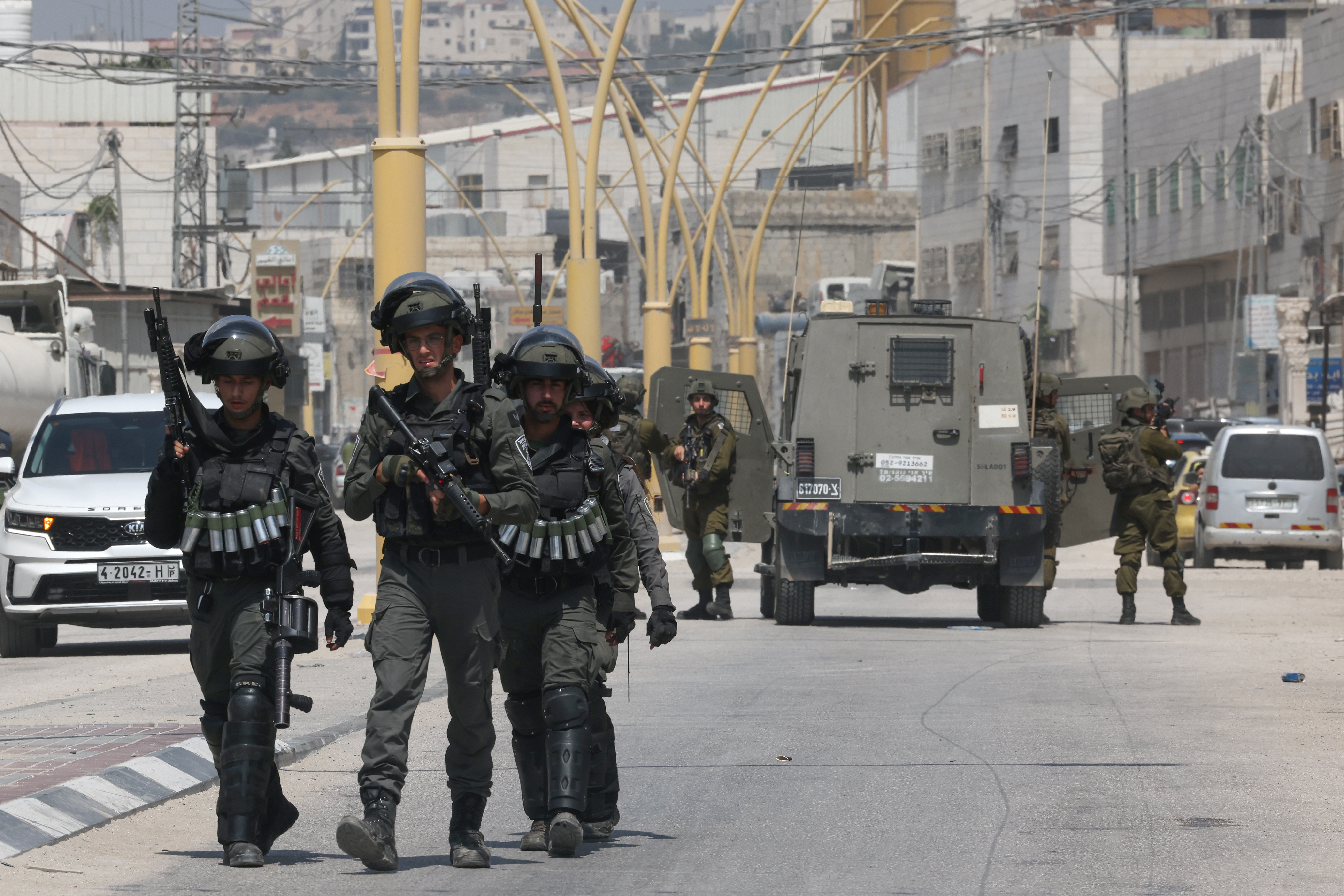 Armored car in road, three soldiers walking towards the camera