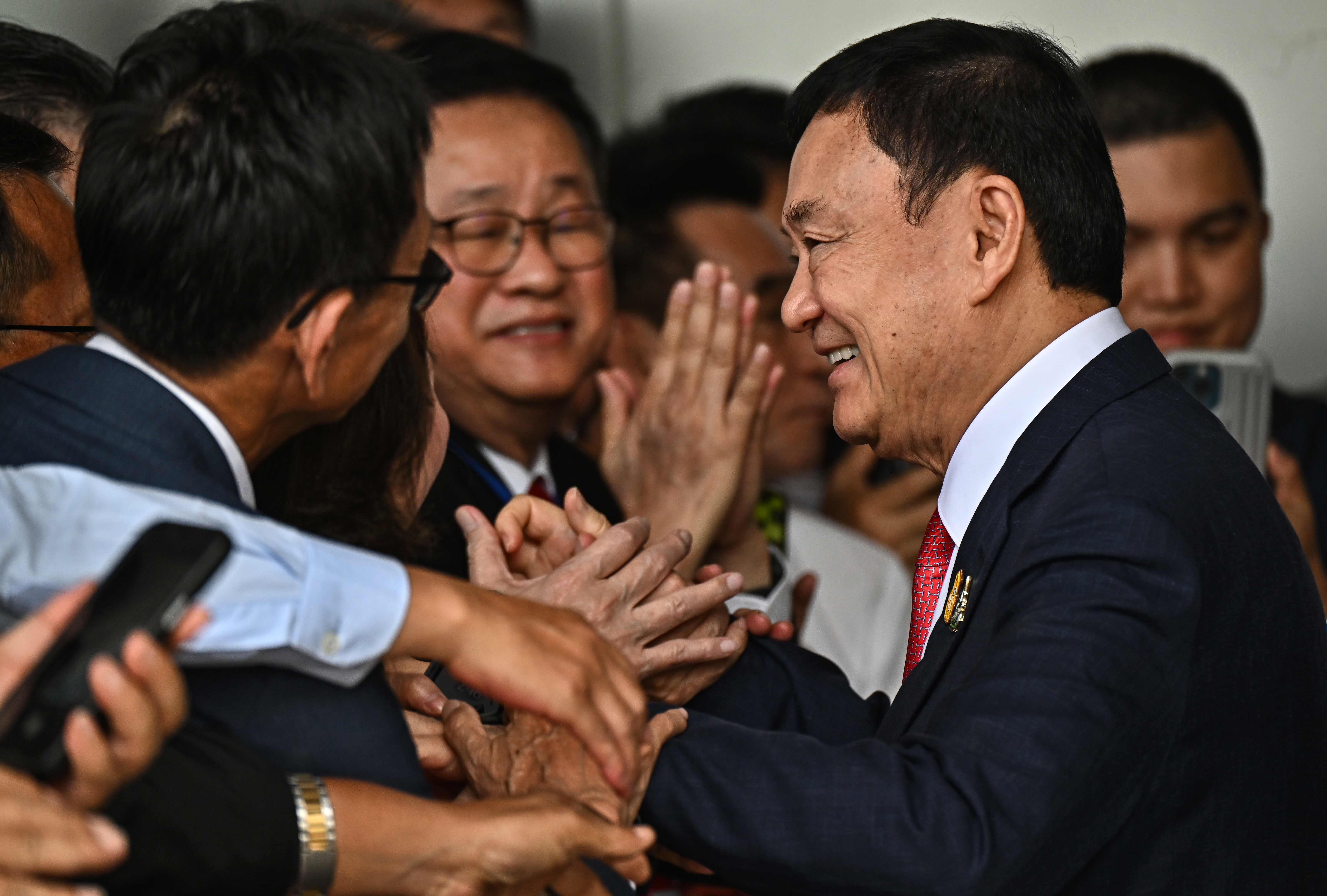 Thaksin smiling and shaking hands with supporters after arriving in Bangkok. Everyone looks happy.