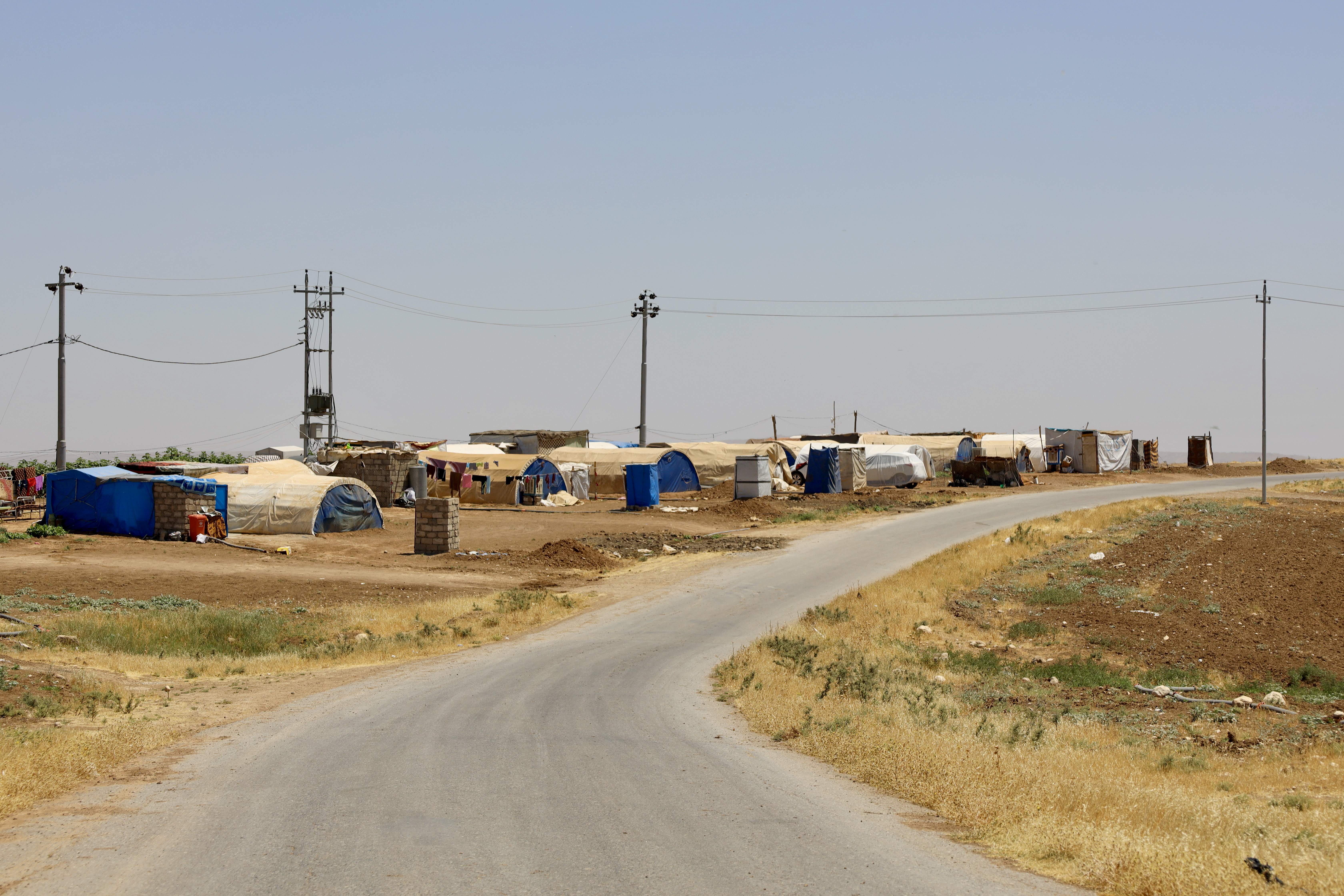A row of tents along a road lined with yellowed grass