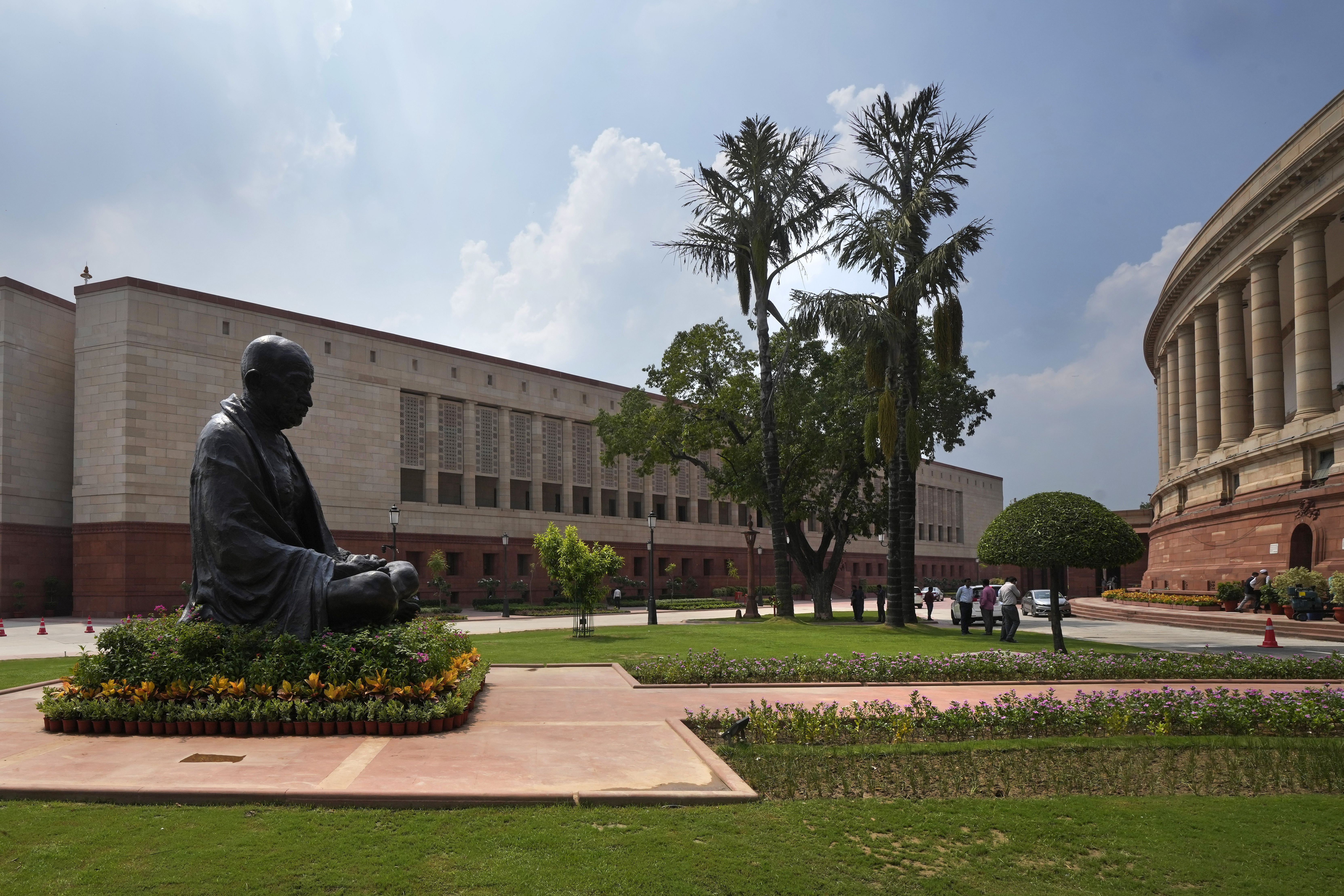 A statue of Mahatma Gandhi sits between the old and new Parliament House buildings on the opening day of the monsoon session of the Indian parliament, in New Delhi, India