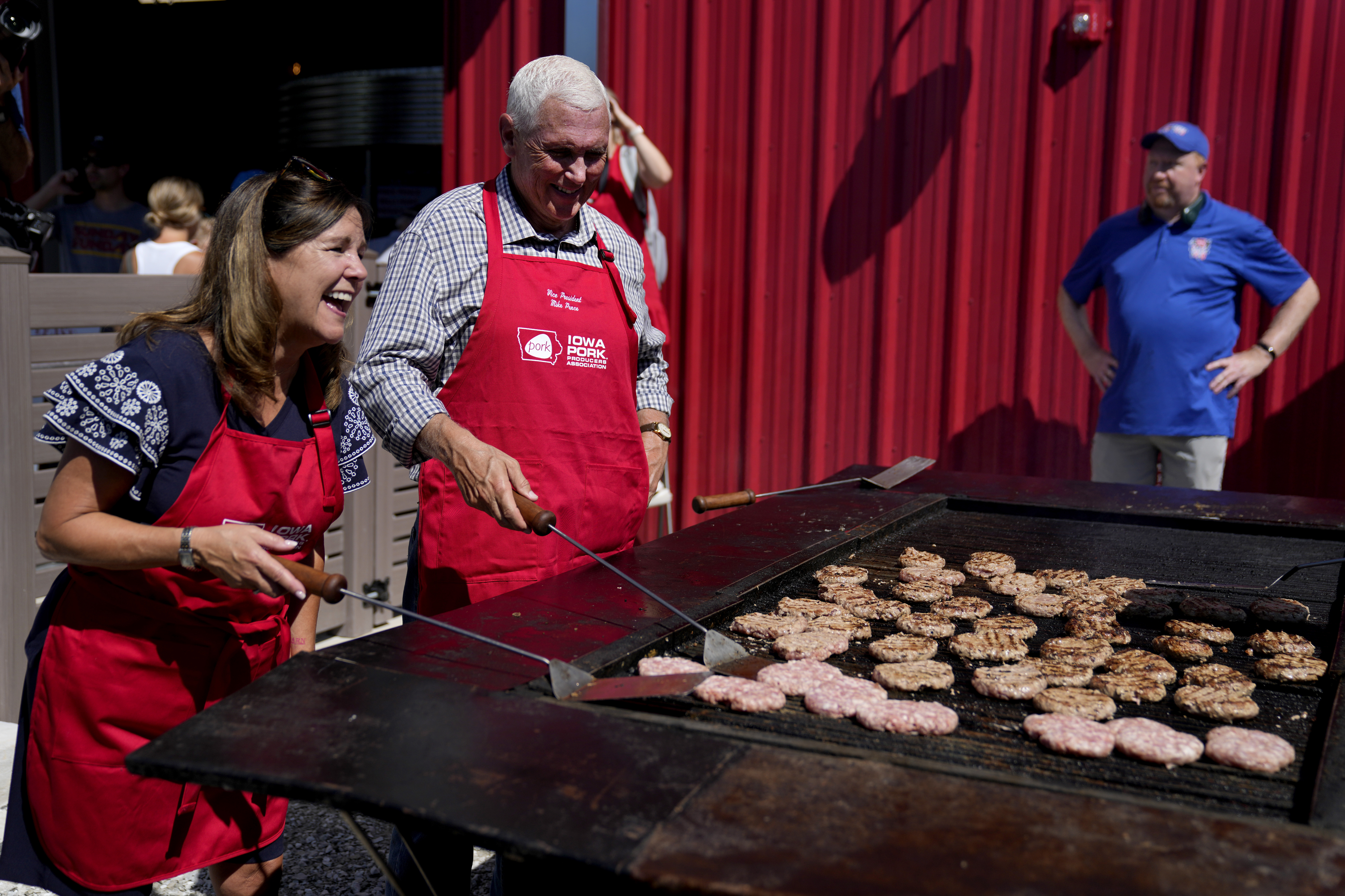 A couple — Mike and Karen Pence — don red aprons and flip pork chops on a large grill.
