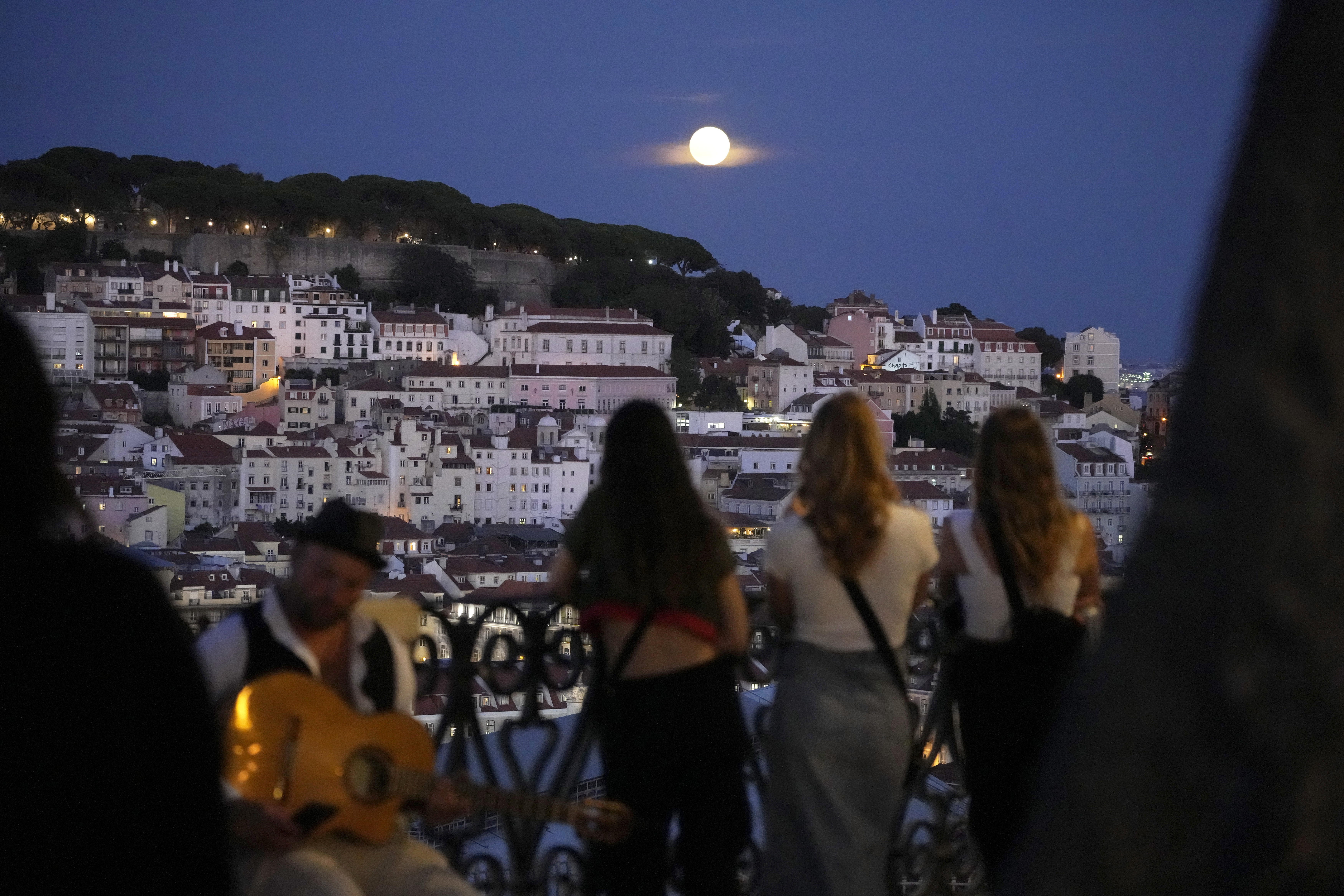 People watch a supermoon rise above Lisbon