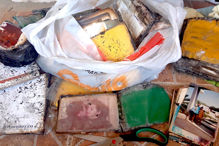 A photo of a plastic bag with damaged and burned photographs with some other damaged and burned photographs around it.