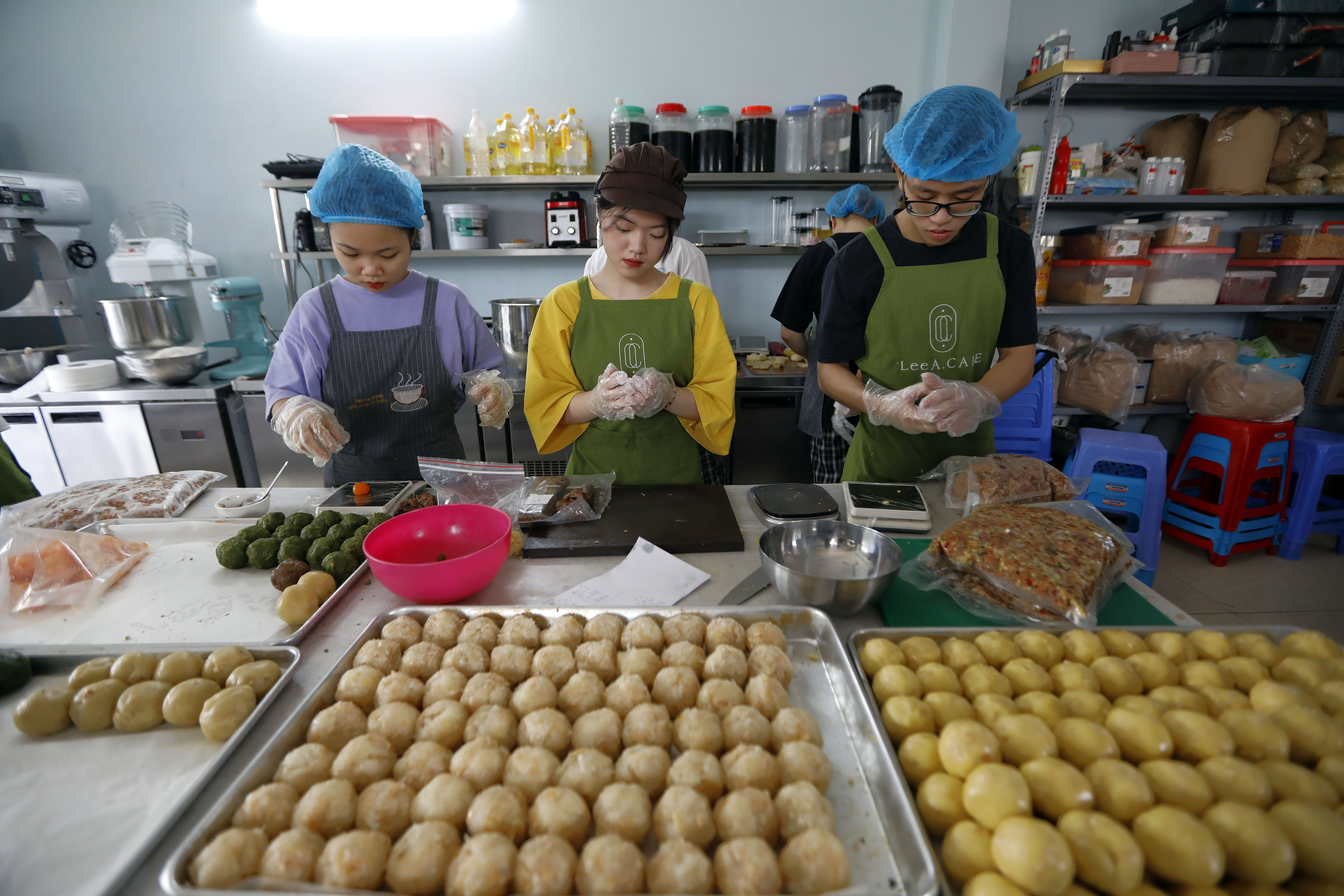 Workers in a bakery in Hanoi prepare mooncakes. The pastries are on a large tray in front of them ready to be shaped.