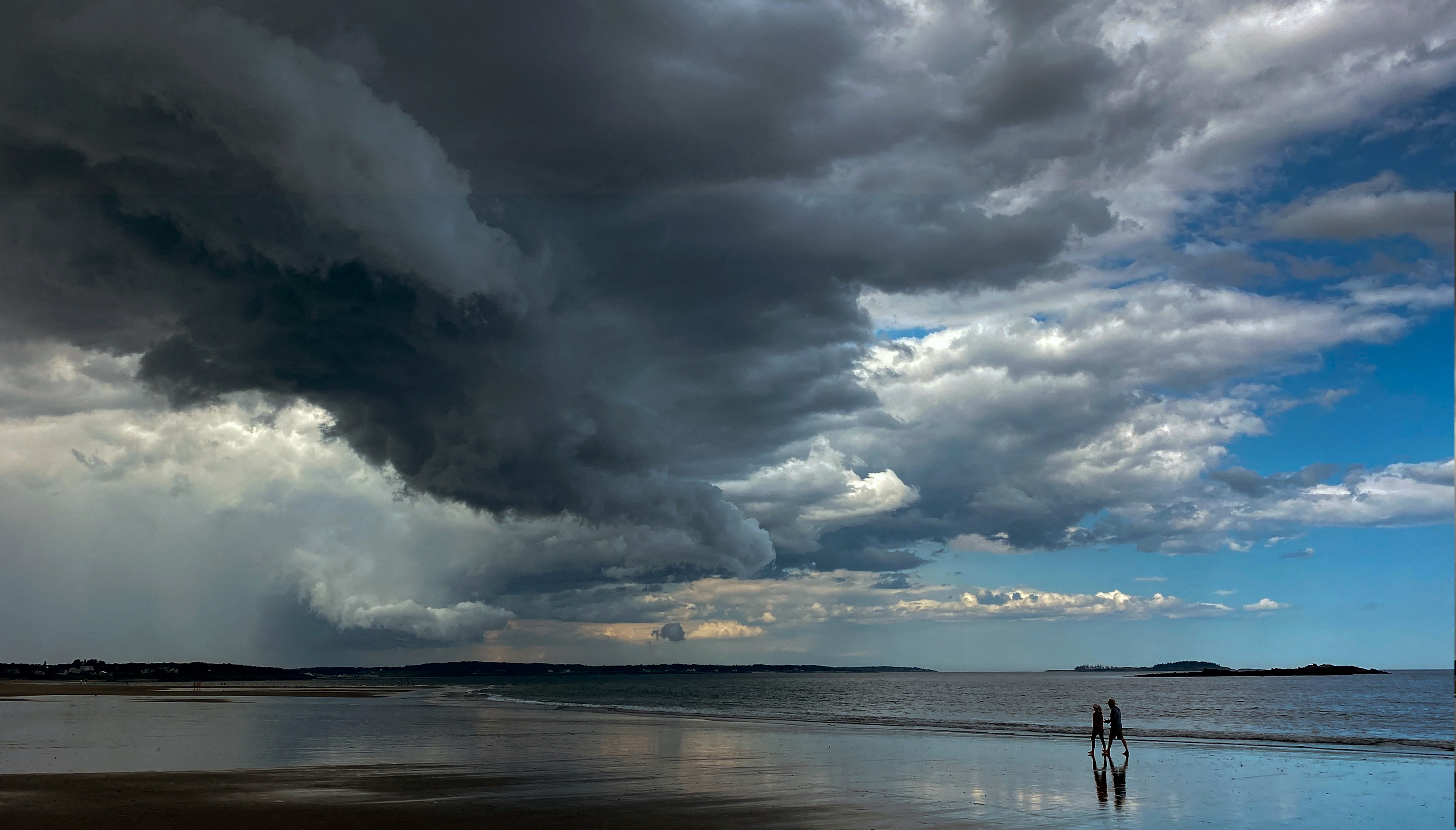People walk along Scarborough Beach under dark clouds in Scarborough, Maine, U.S, July 31, 2023. REUTERS/Kevin Lamarque