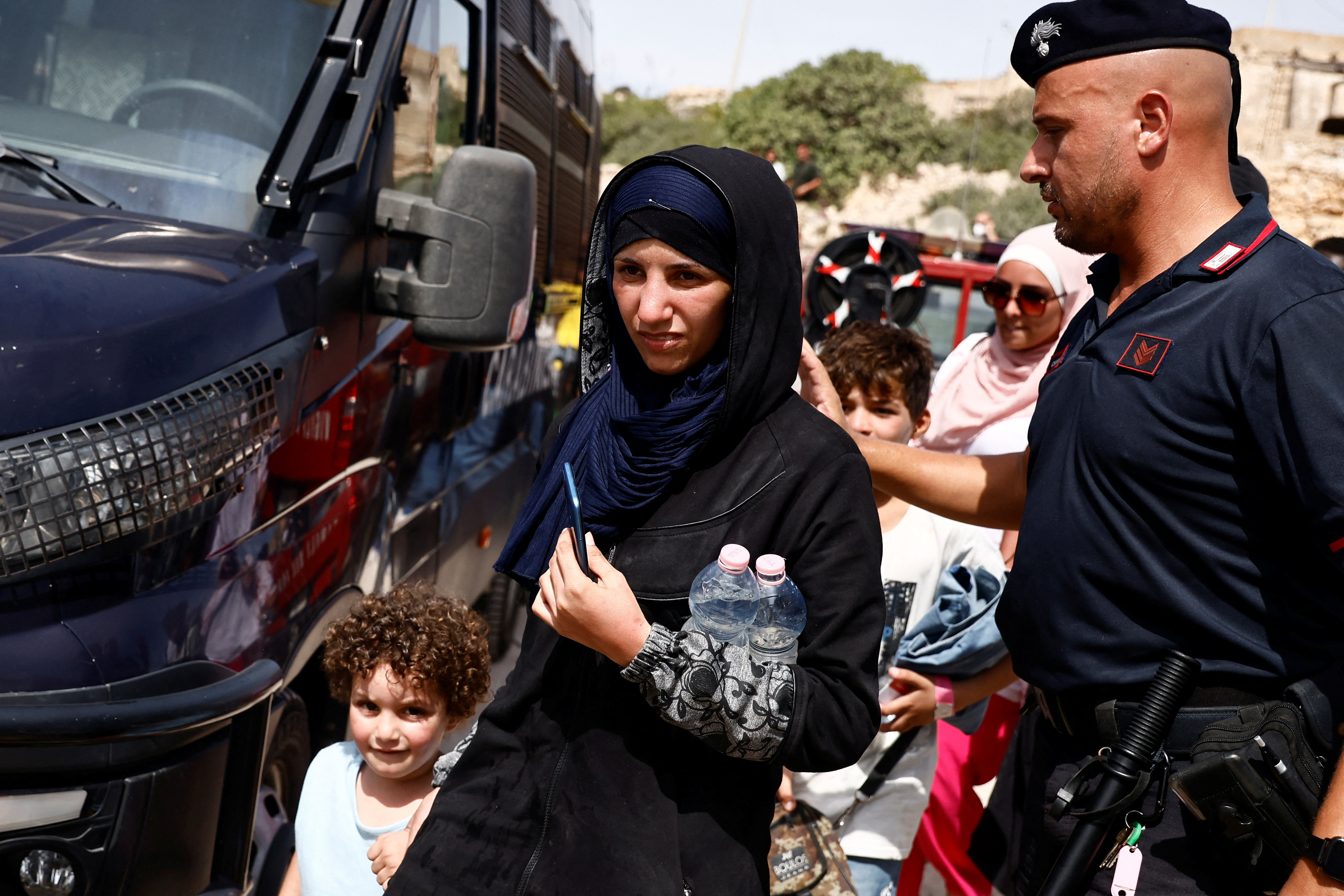 Migrants walks past a member of the Carabinieri outside the hotspot, on the Sicilian island of Lampedusa, Italy